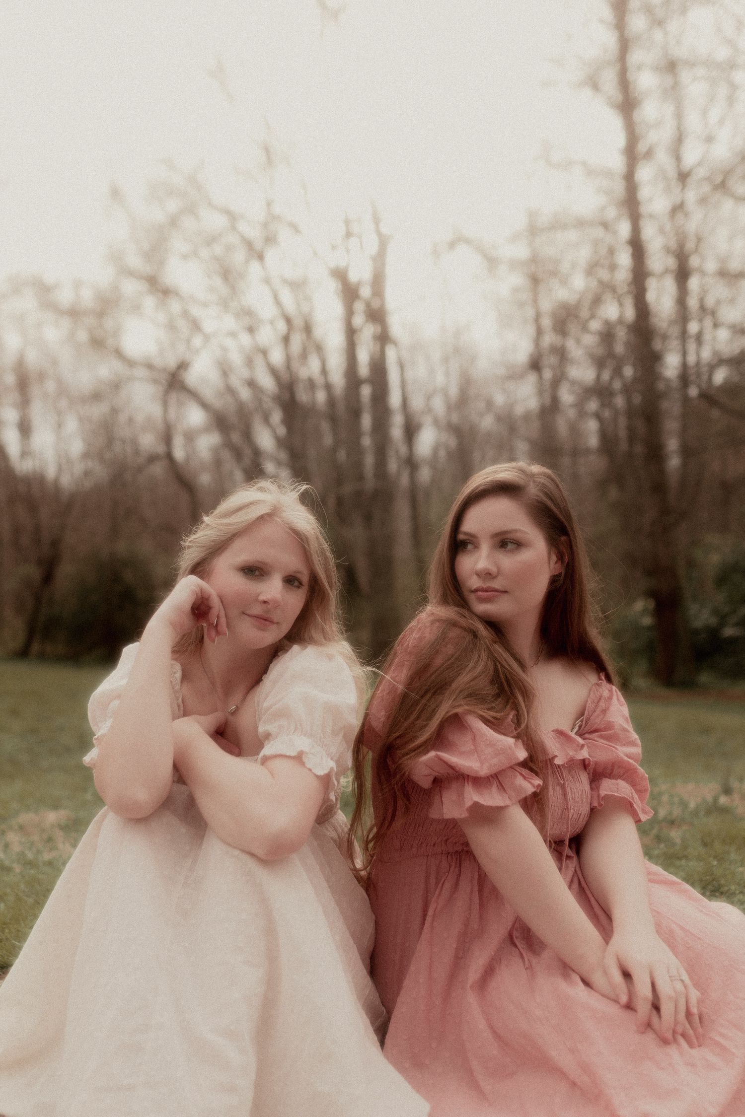Romantic portrait of two people in vintage-style dresses posed in dreamy outdoor setting.