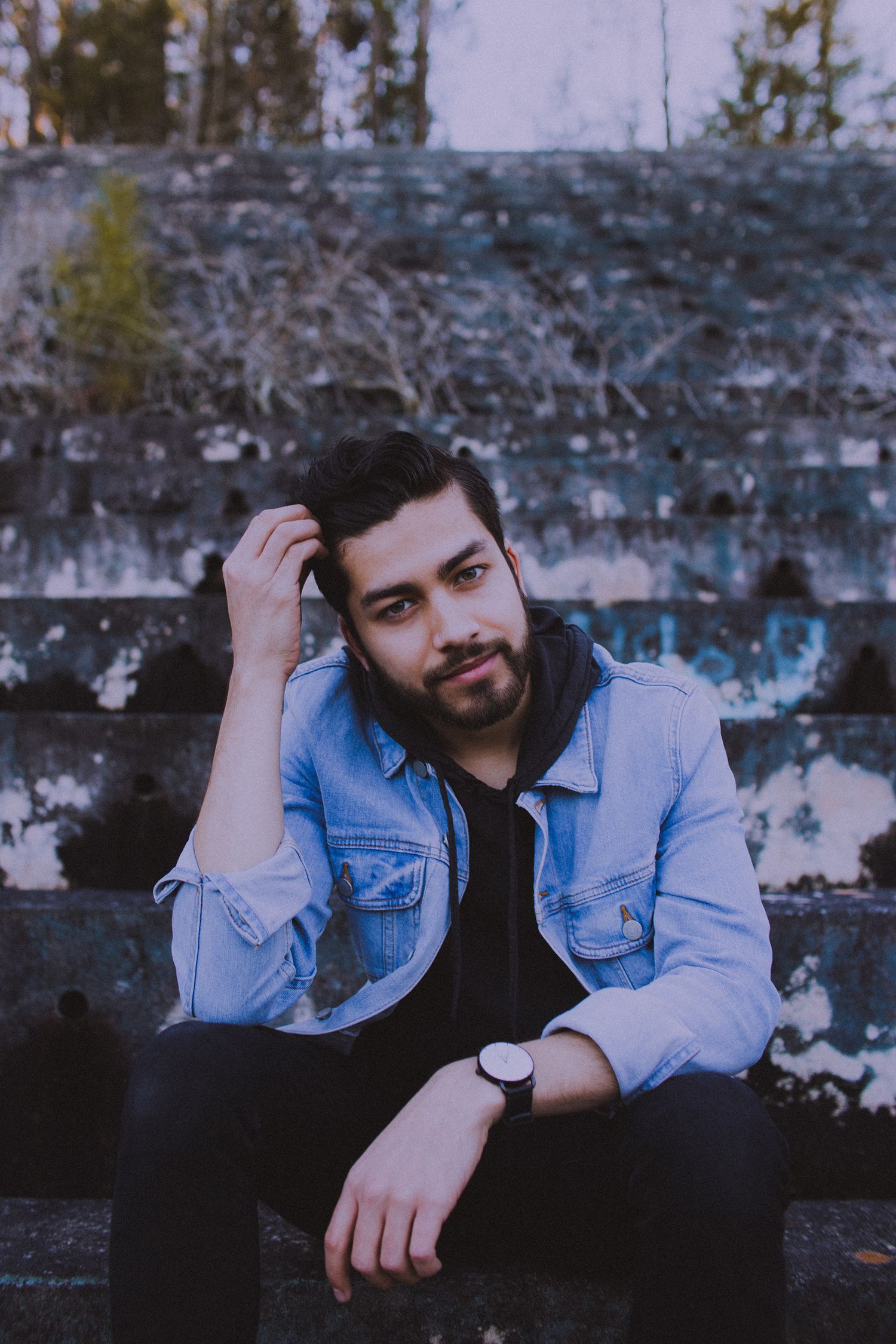 Portrait series against blue wall showing casual poses in denim jacket and dark clothing.