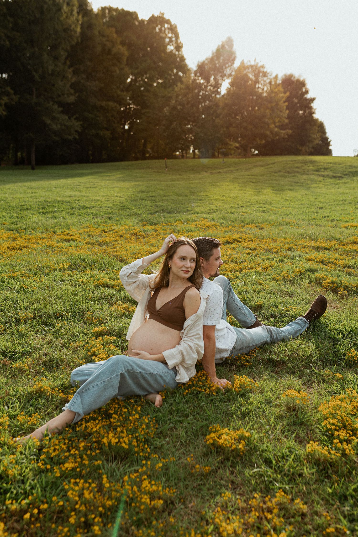 Couple relaxing on grassy hillside with yellow wildflowers at sunset.
