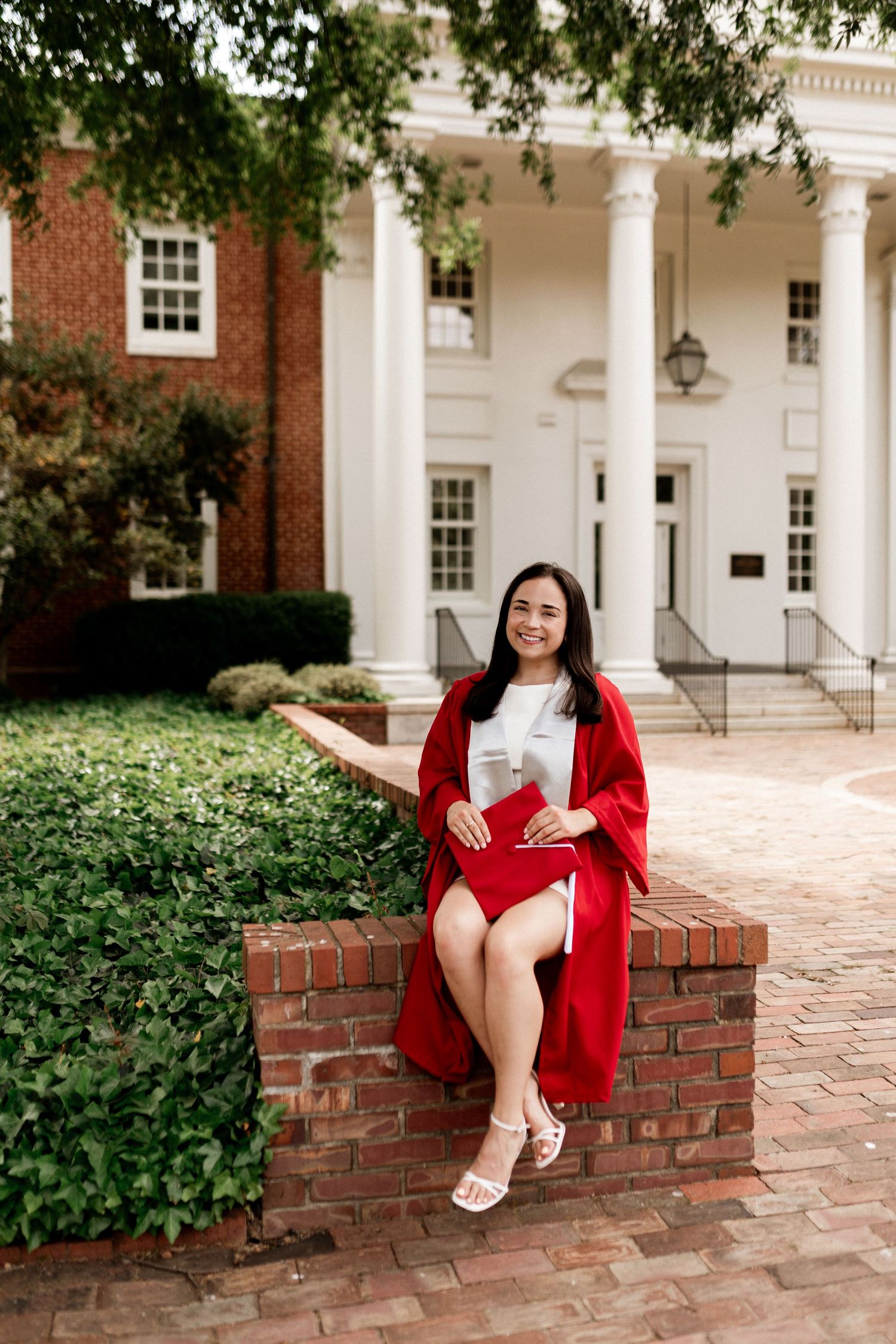 A person in a red blazer sits on a brick wall outside a white columned building.