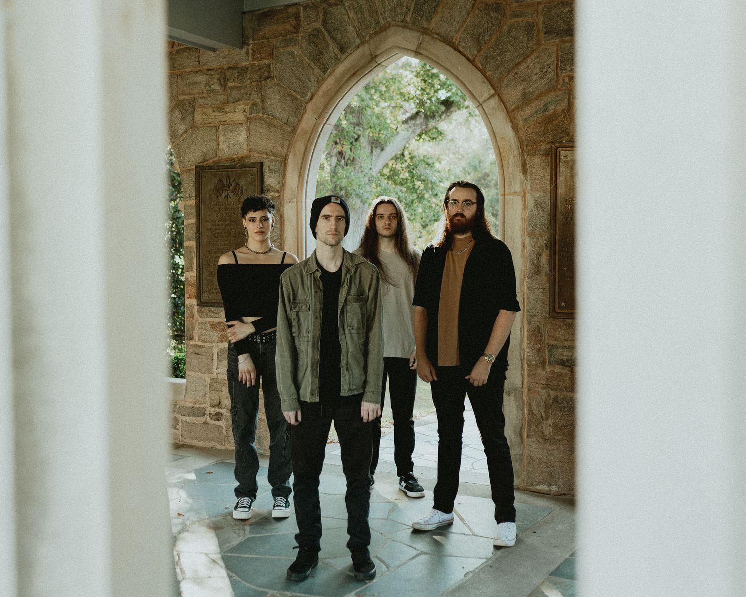 Music group poses under a stone archway in casual attire.