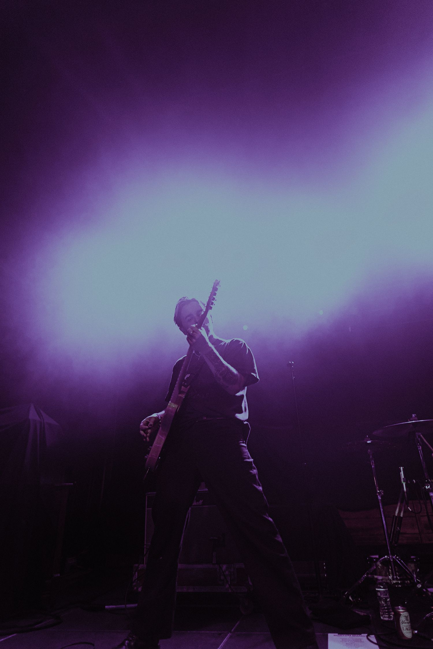 Silhouette of a guitarist performing on stage with dramatic purple lighting and fog effects.