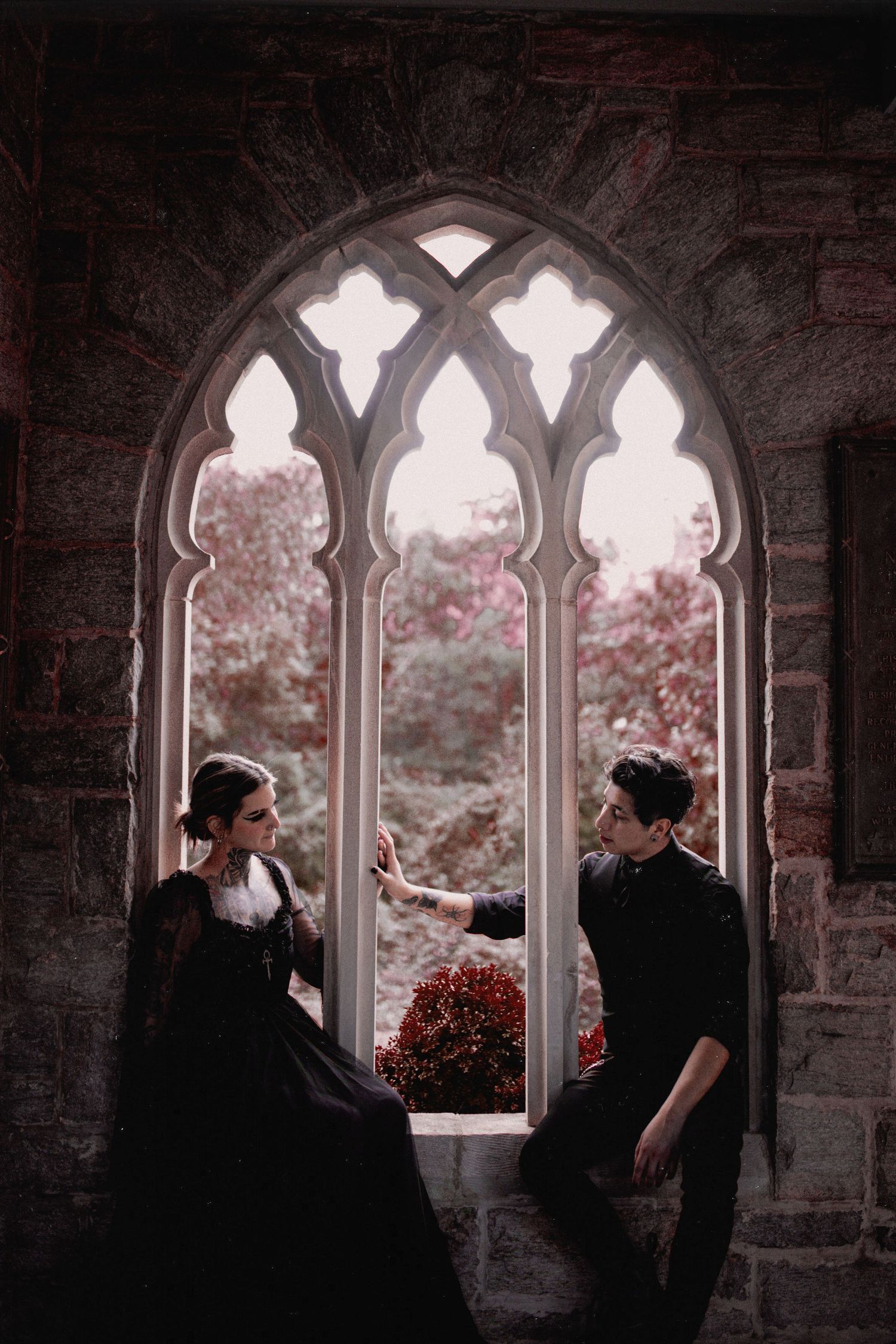 Figures silhouetted against Gothic stone windows with garden view.