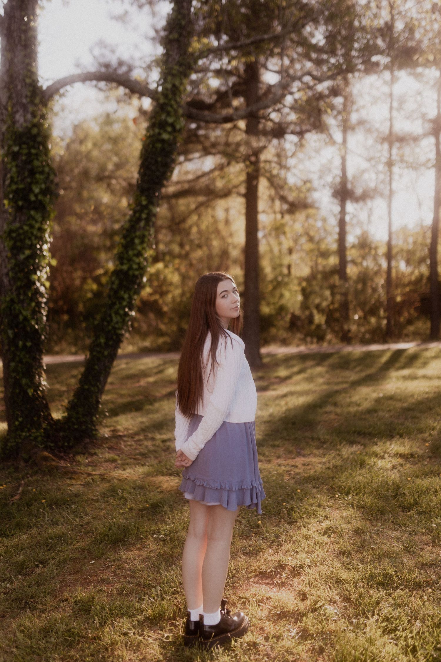 Whimsical forest portrait in purple dress with ivy-covered trees.