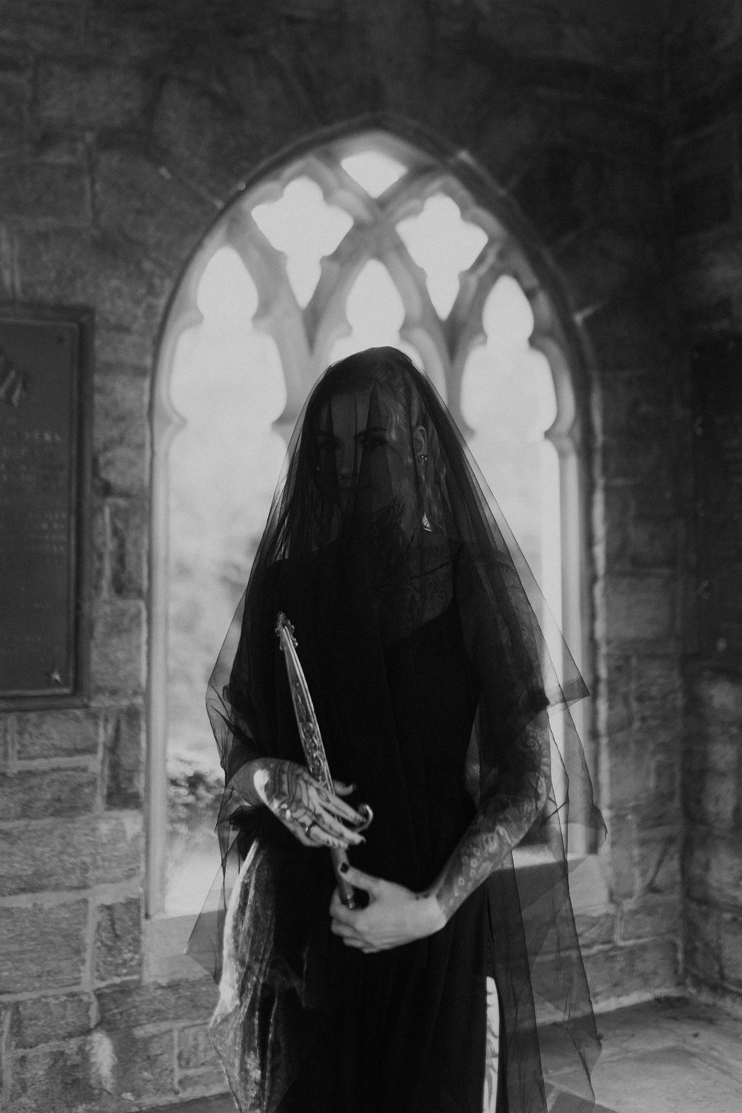 Gothic figure in black veil standing in church archway holding mysterious object.