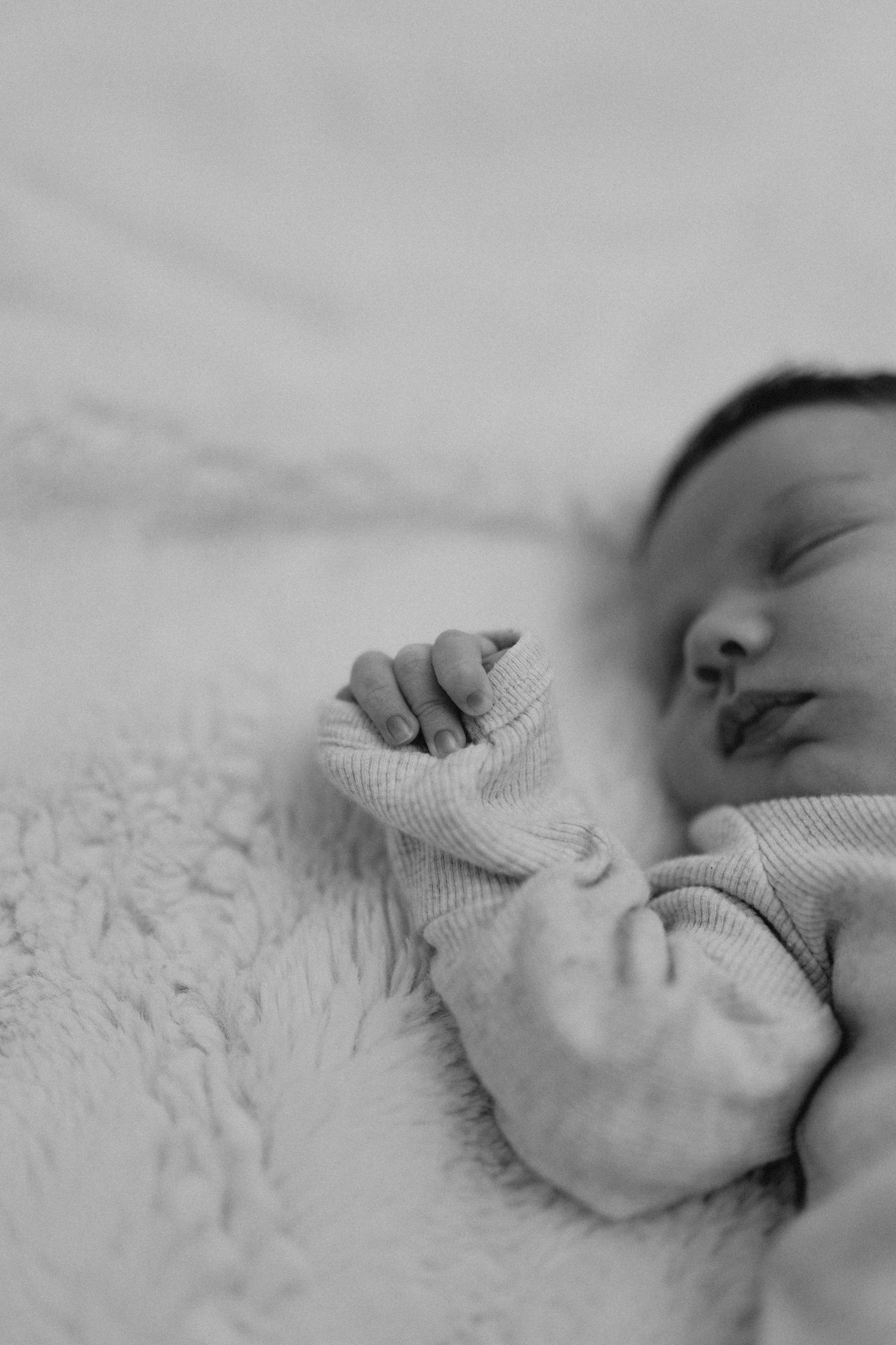 Close-up black and white photo of a sleeping newborn's tiny hand grasping fabric.