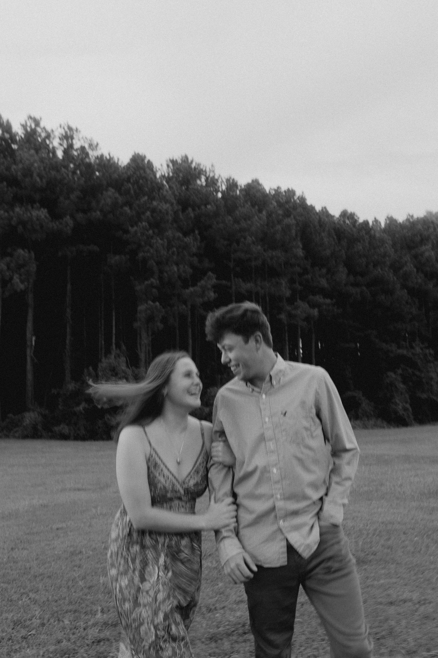 A couple laughs together during a black and white photoshoot in a meadow.