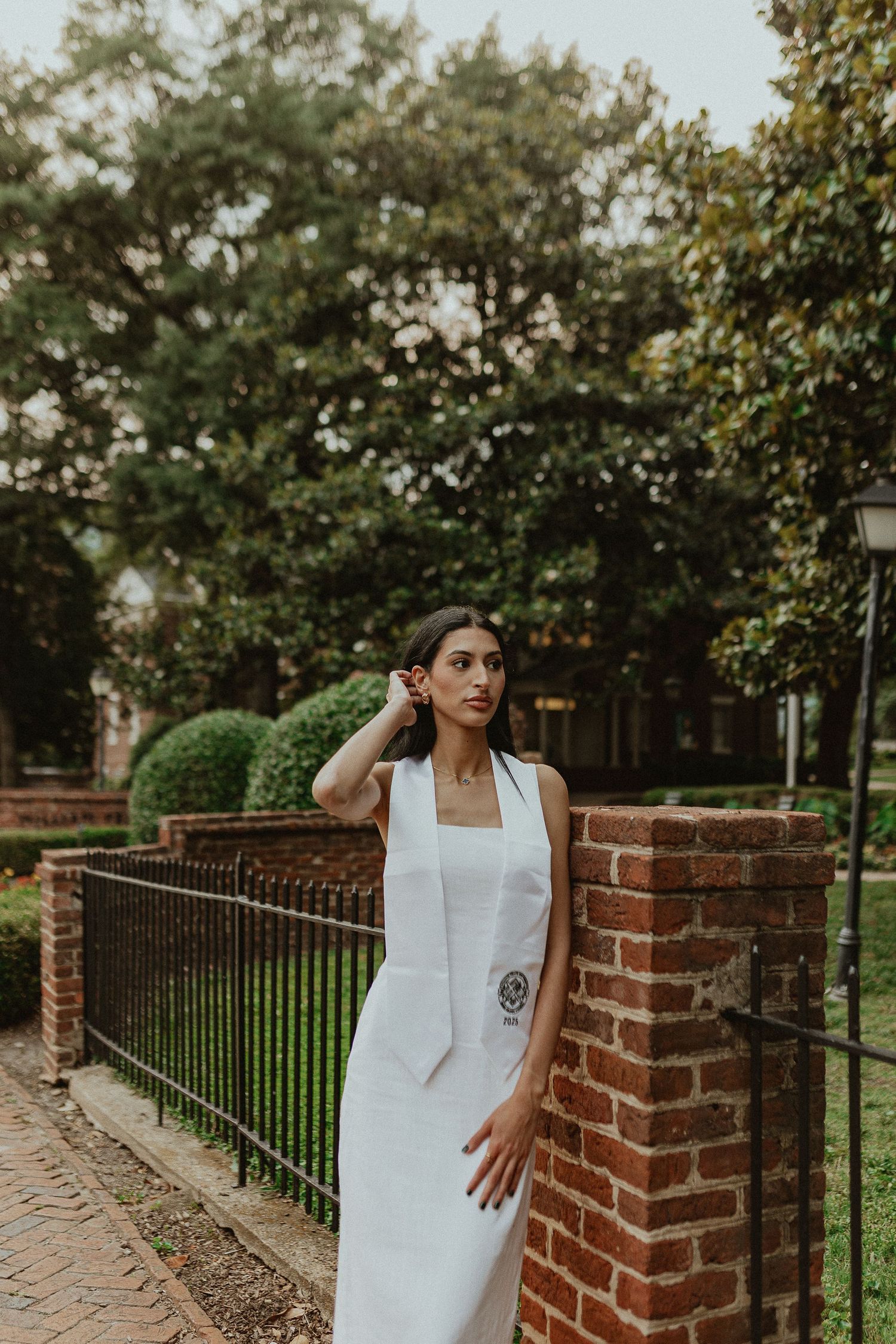 White dress against brick wall and iron fence in garden setting.