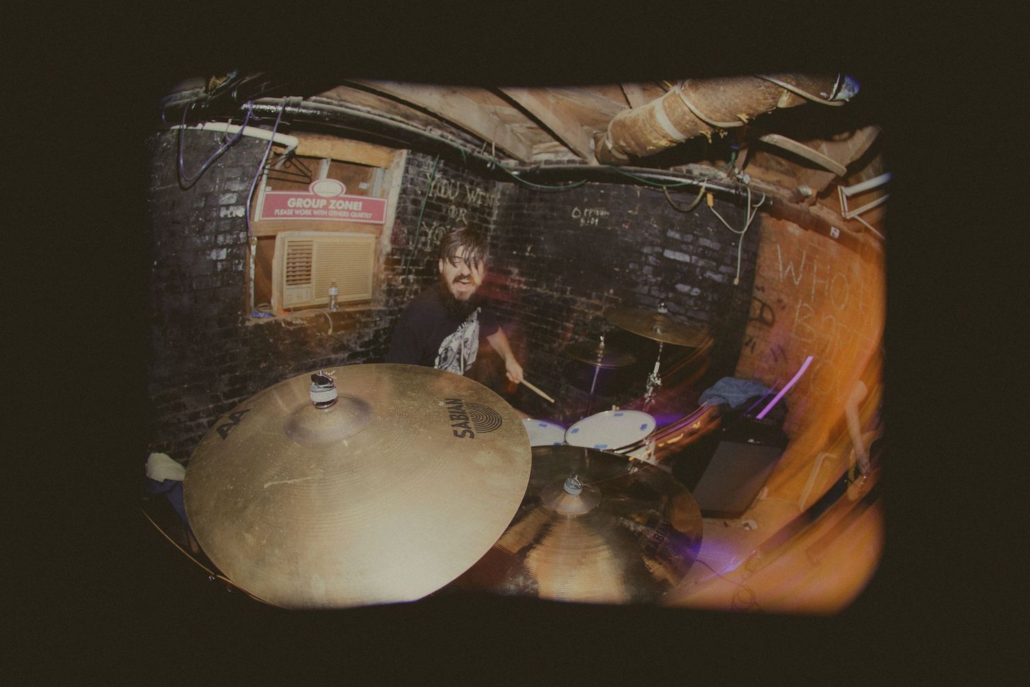Concert venue setup with drum kit and equipment visible under warm stage lighting.