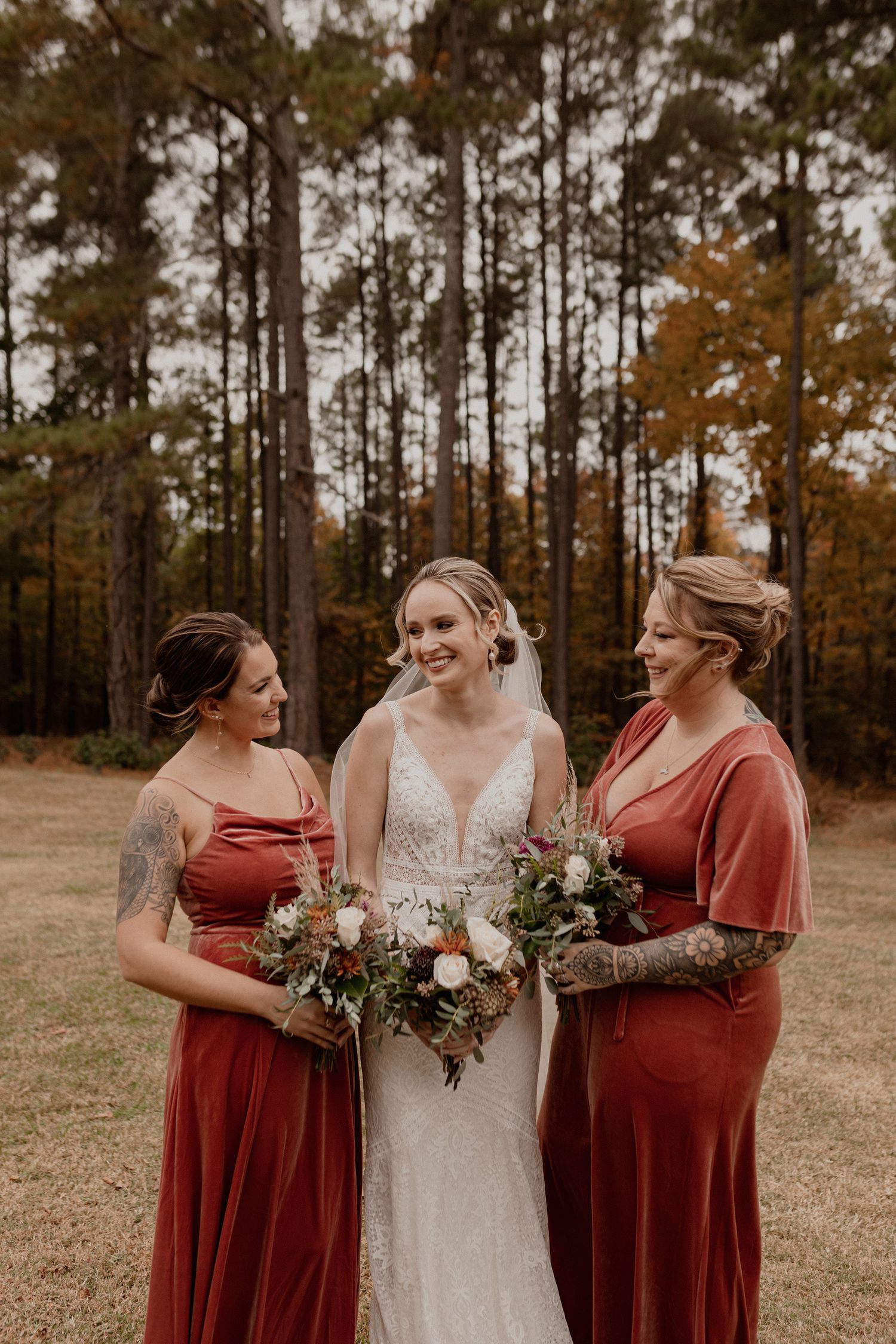 Wedding party poses in burgundy dresses and white gown against autumn forest backdrop.