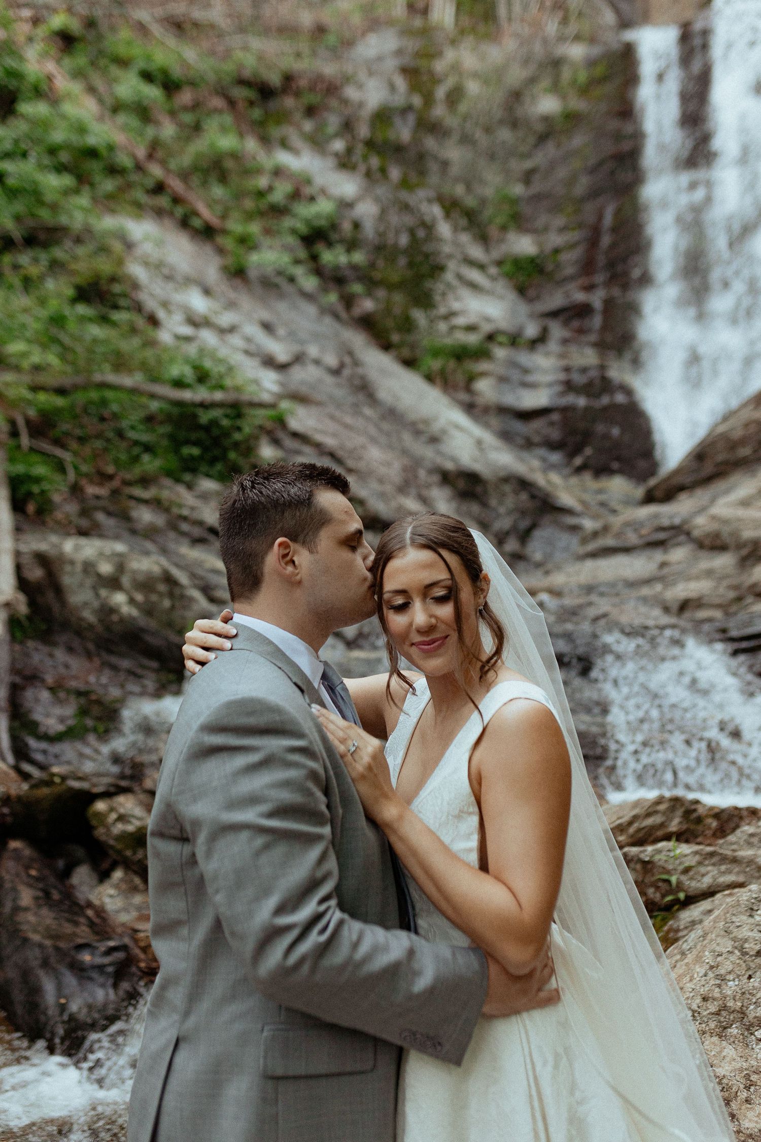 A couple shares an intimate moment in front of a cascading waterfall.