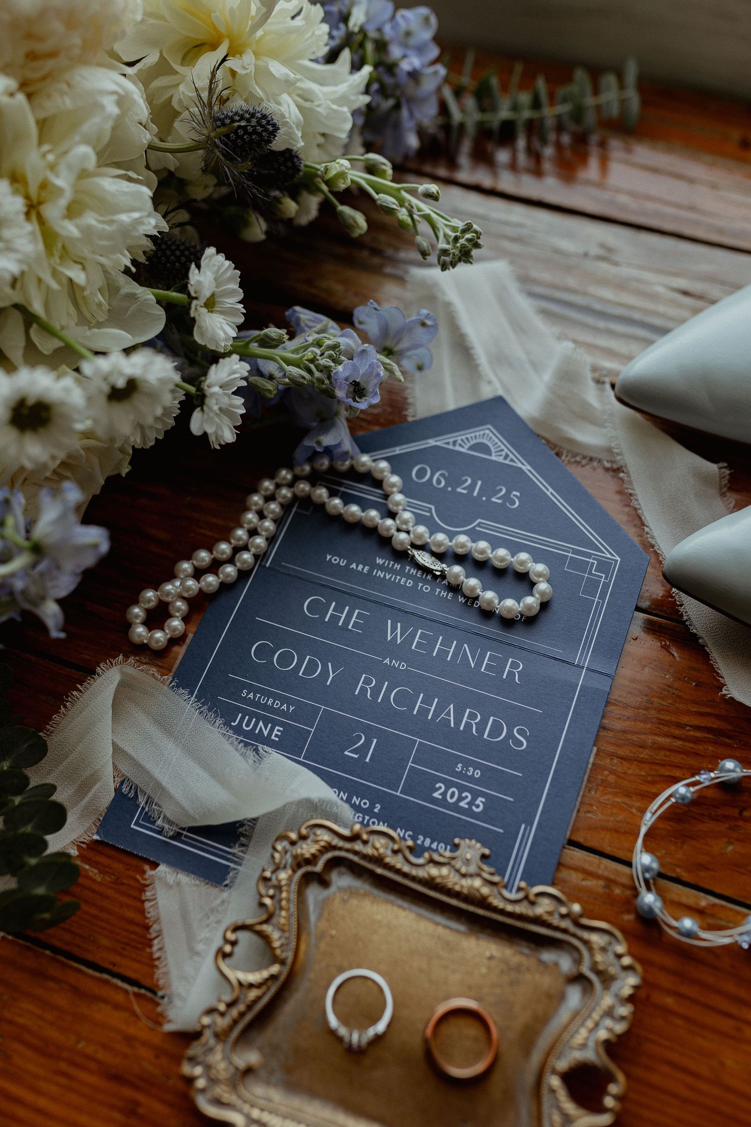 Wedding details including name cards, pearls, and white flowers arranged on wooden surface.