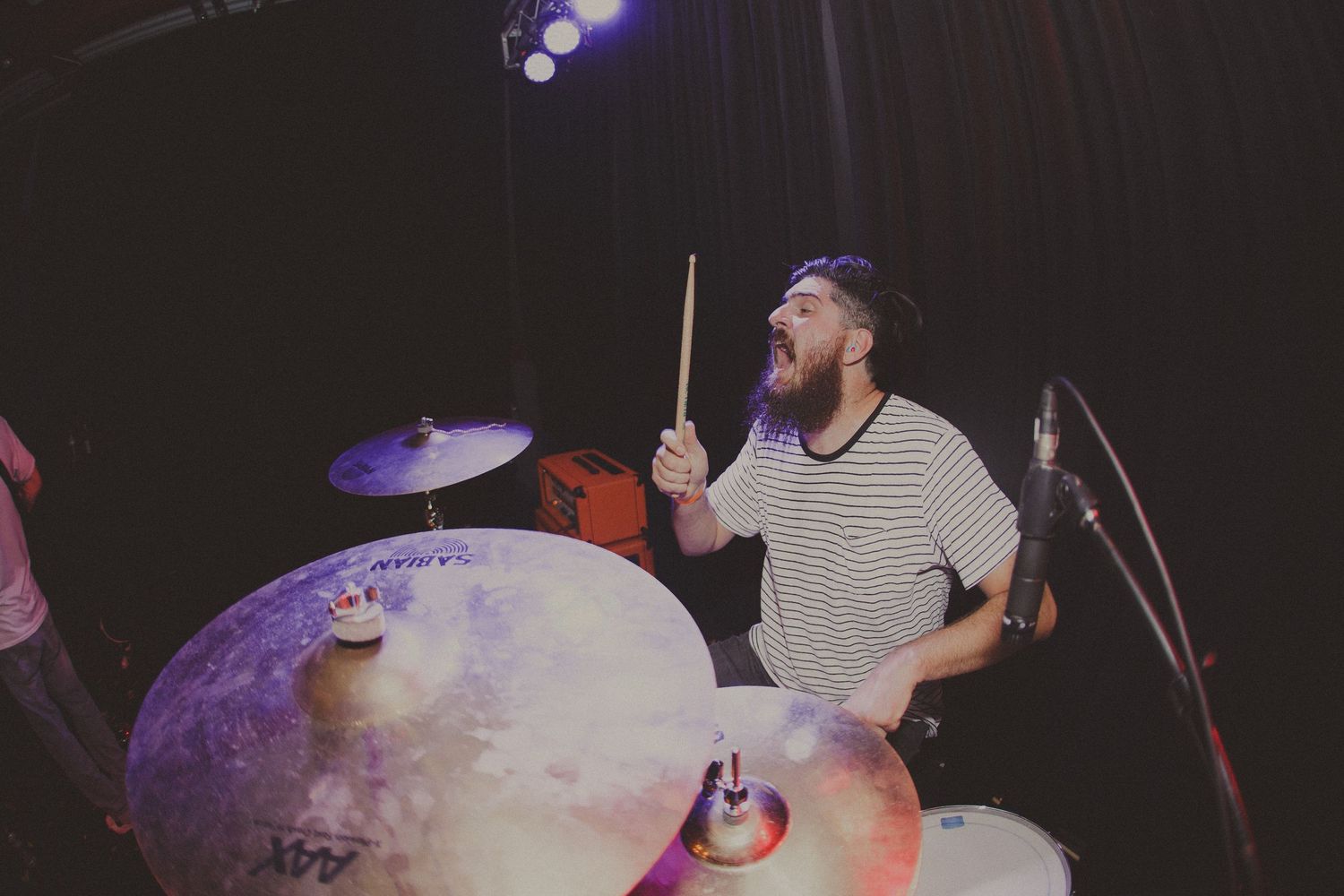 Drummer performing behind a drum kit with purple stage lighting in the background.