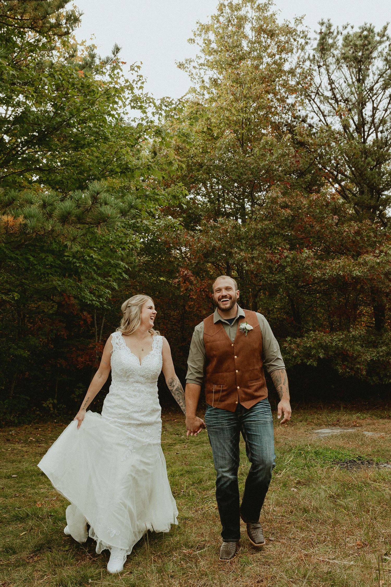 A couple walking hand in hand through an autumn field in wedding attire.