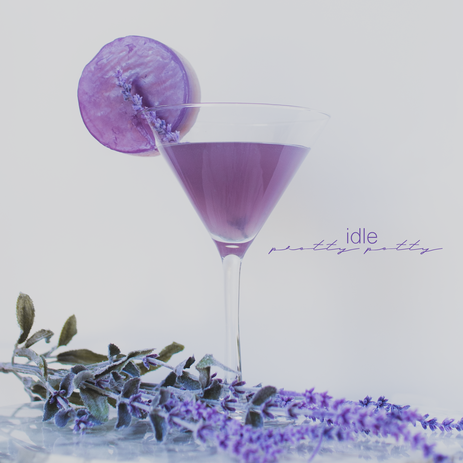 Purple cocktail glass with lavender sprigs arranged in minimalist composition.