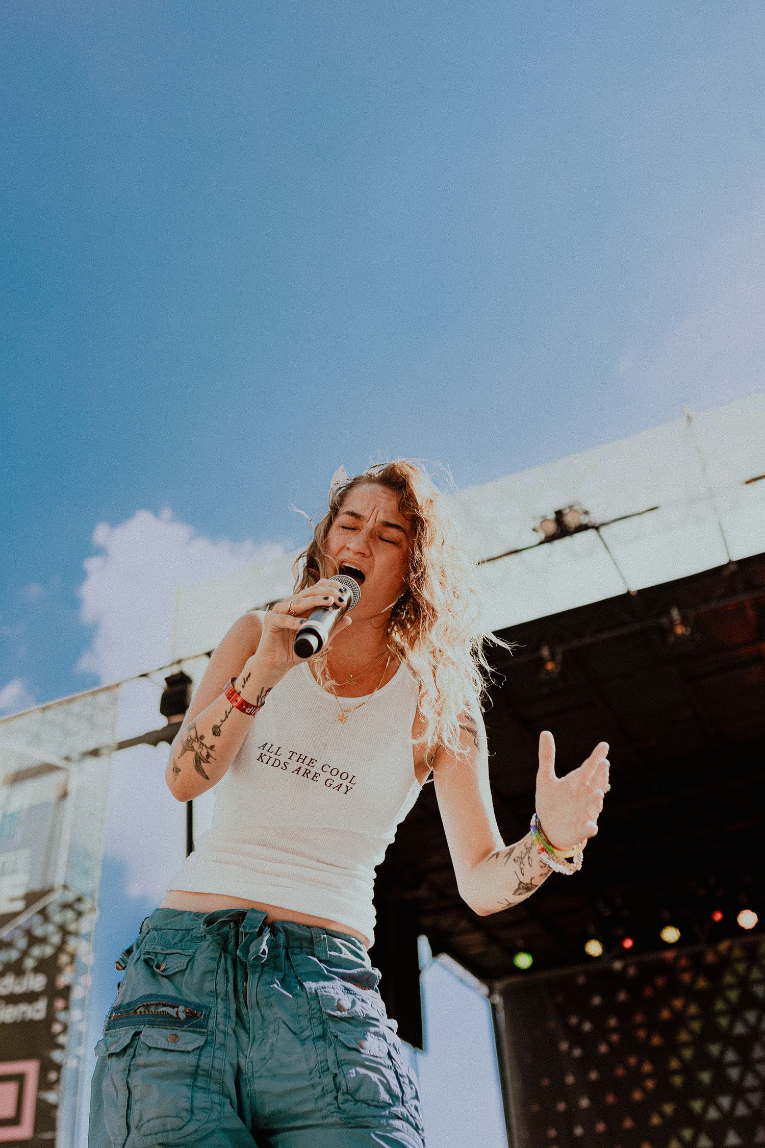 A performer sings passionately on an outdoor stage during a daytime concert.