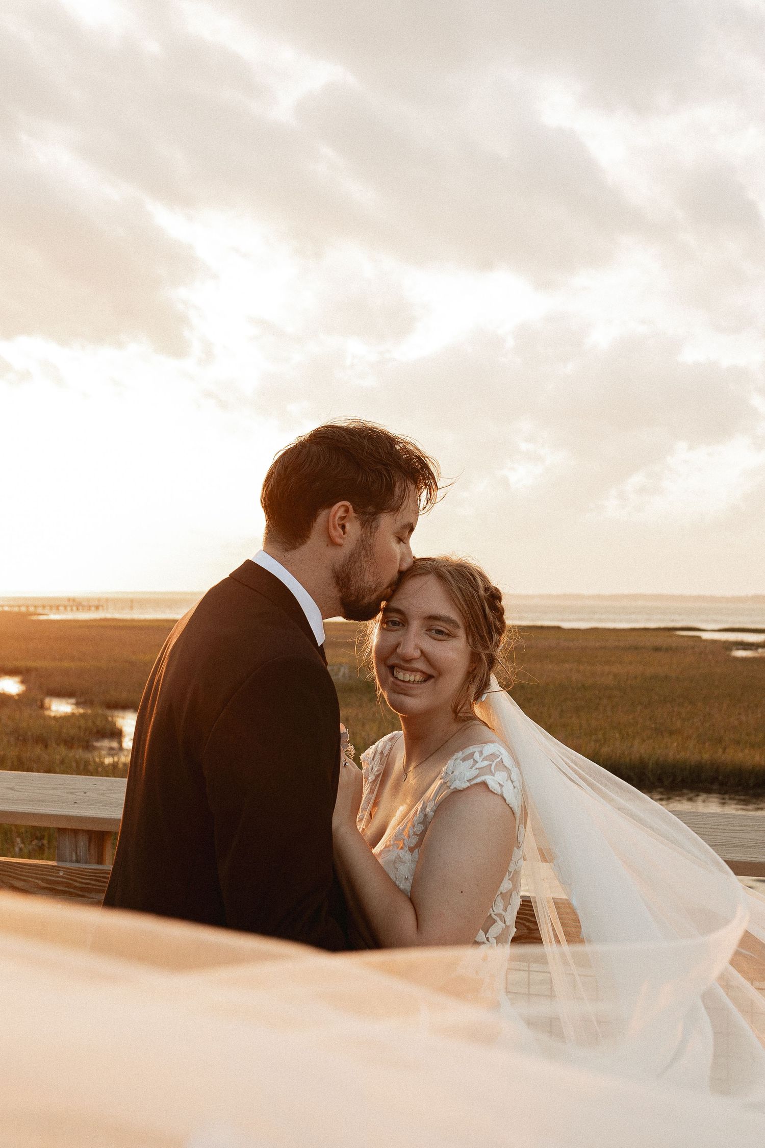 A sunset wedding portrait shows a couple sharing a tender moment with marshland in the background.
