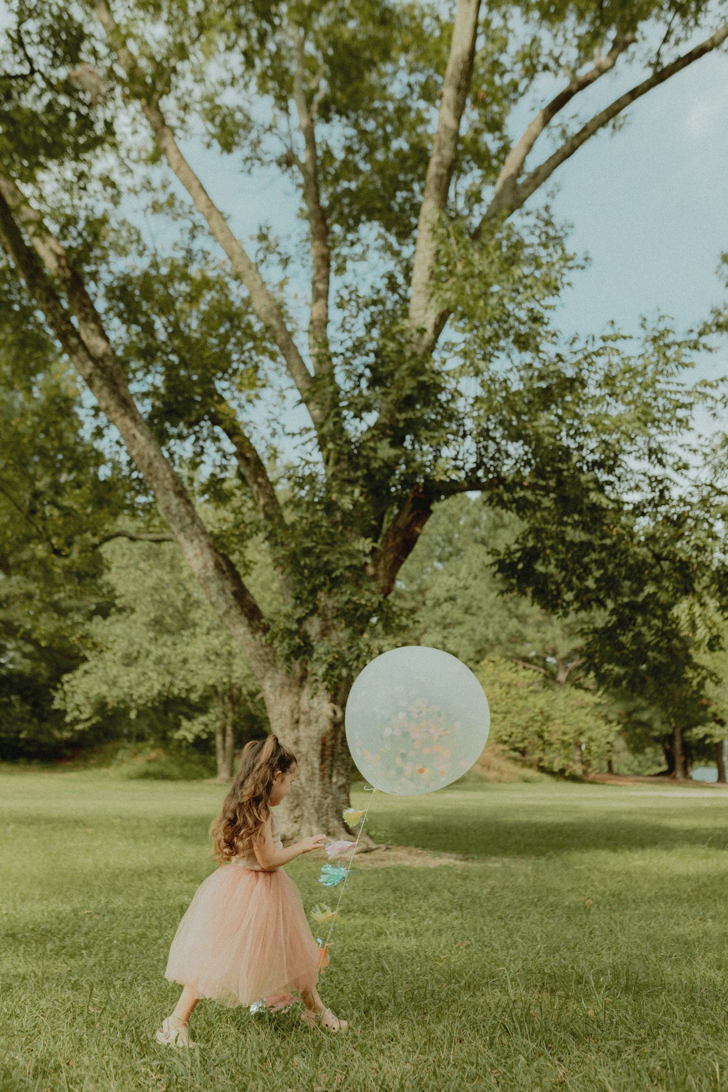 A child in pink dress chases bubbles in a sunny park setting.