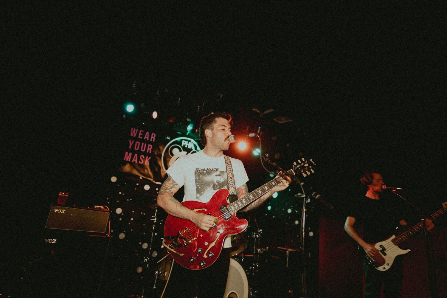 Musician playing red electric guitar on dark stage with concert lighting.
