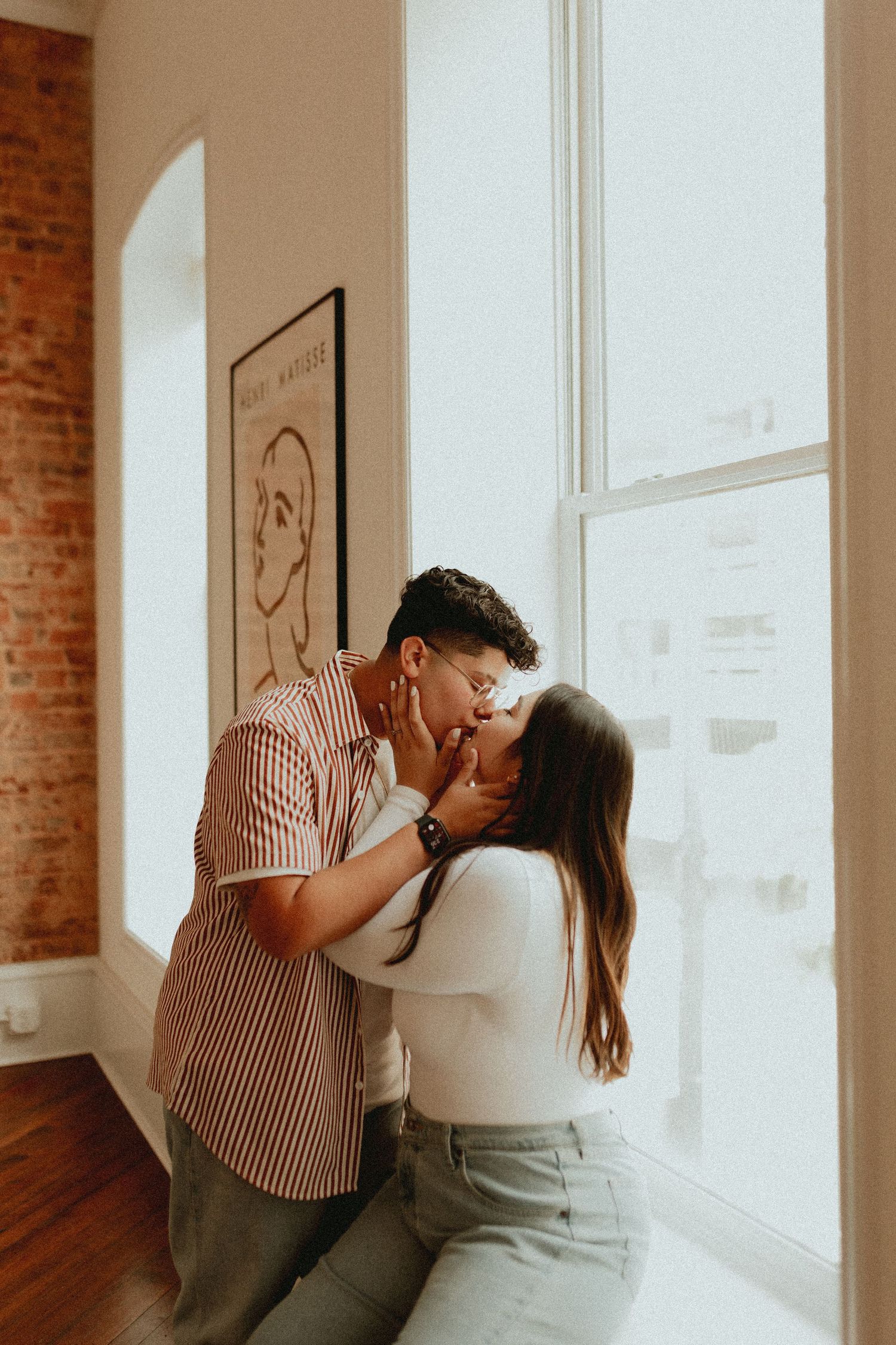 Intimate indoor photoshoot with natural window light and exposed brick wall details.