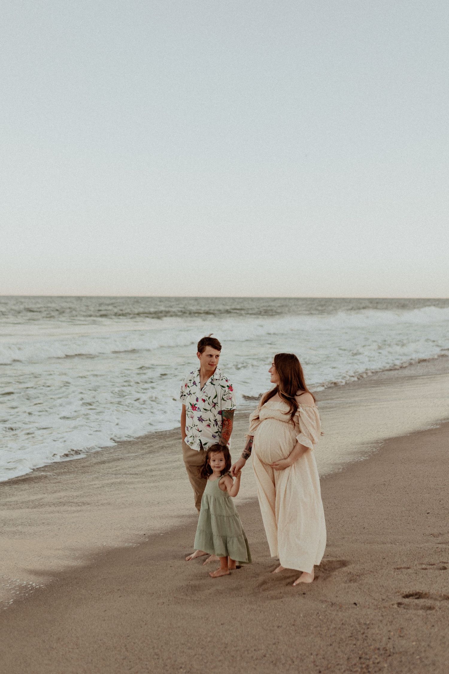 Family walks together along peaceful beach shoreline at dusk.