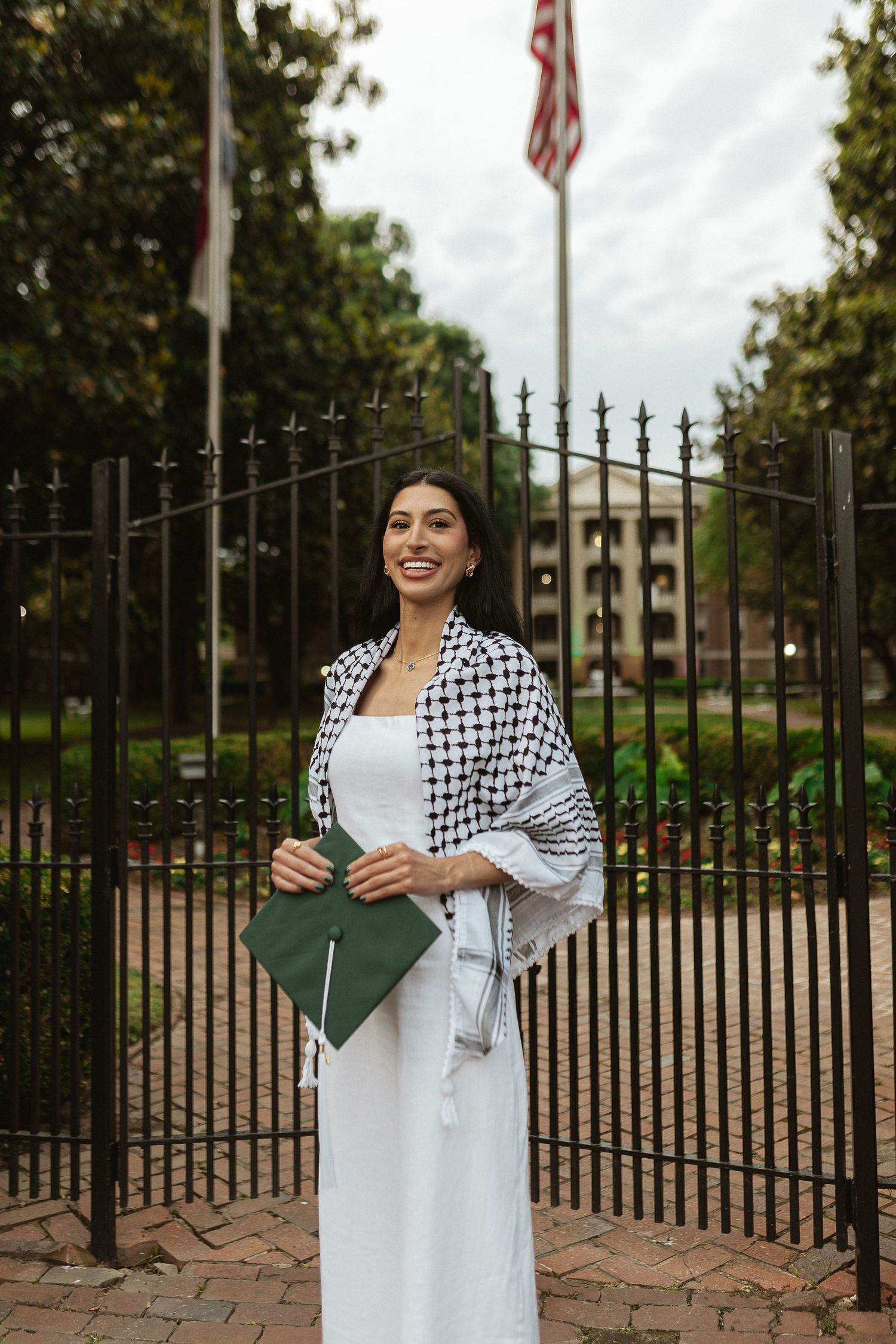 White dress and patterned jacket against iron gates and flagpoles.
