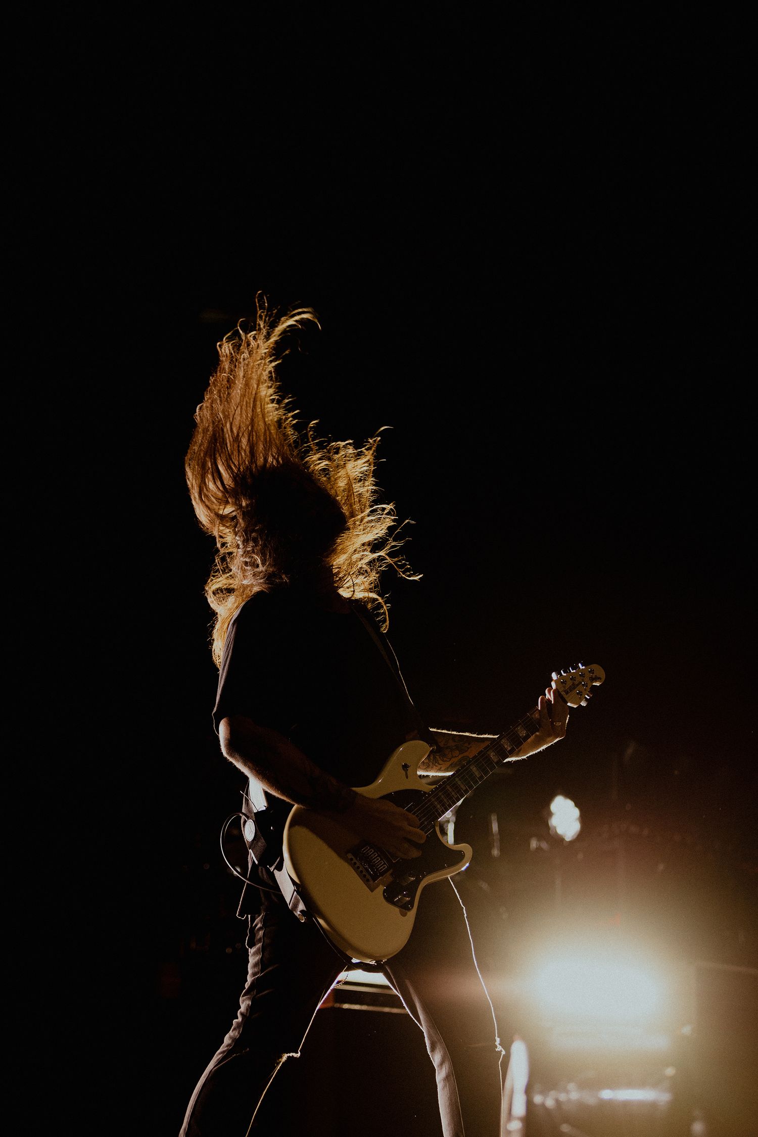 Dramatic concert moment with hair flying and silhouetted figure against warm stage lights.