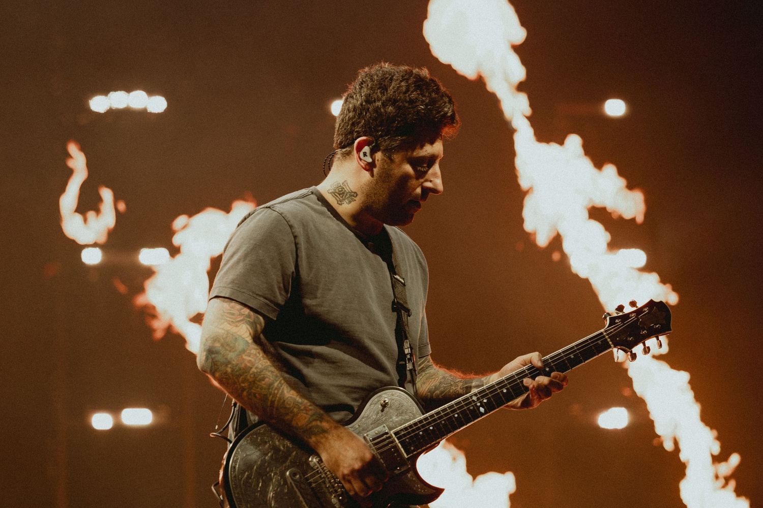 Guitarist performs on stage with dramatic fire pyrotechnics in background.