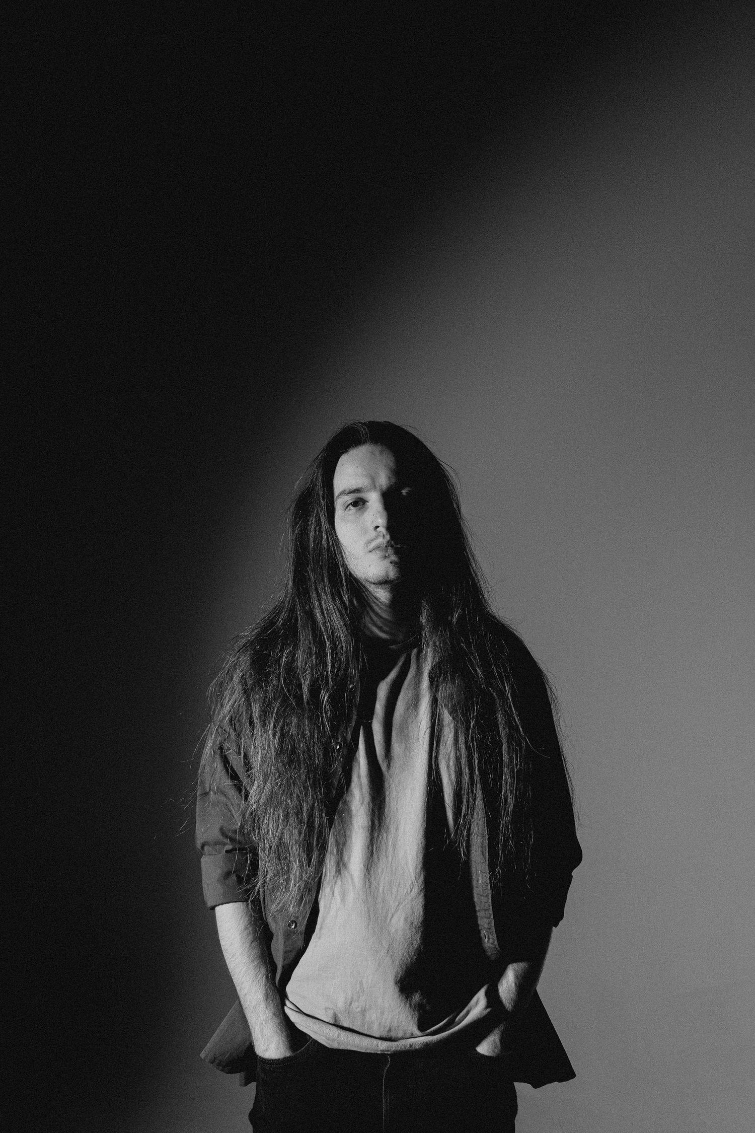 Dramatic black and white portrait with long dark hair against gray background.