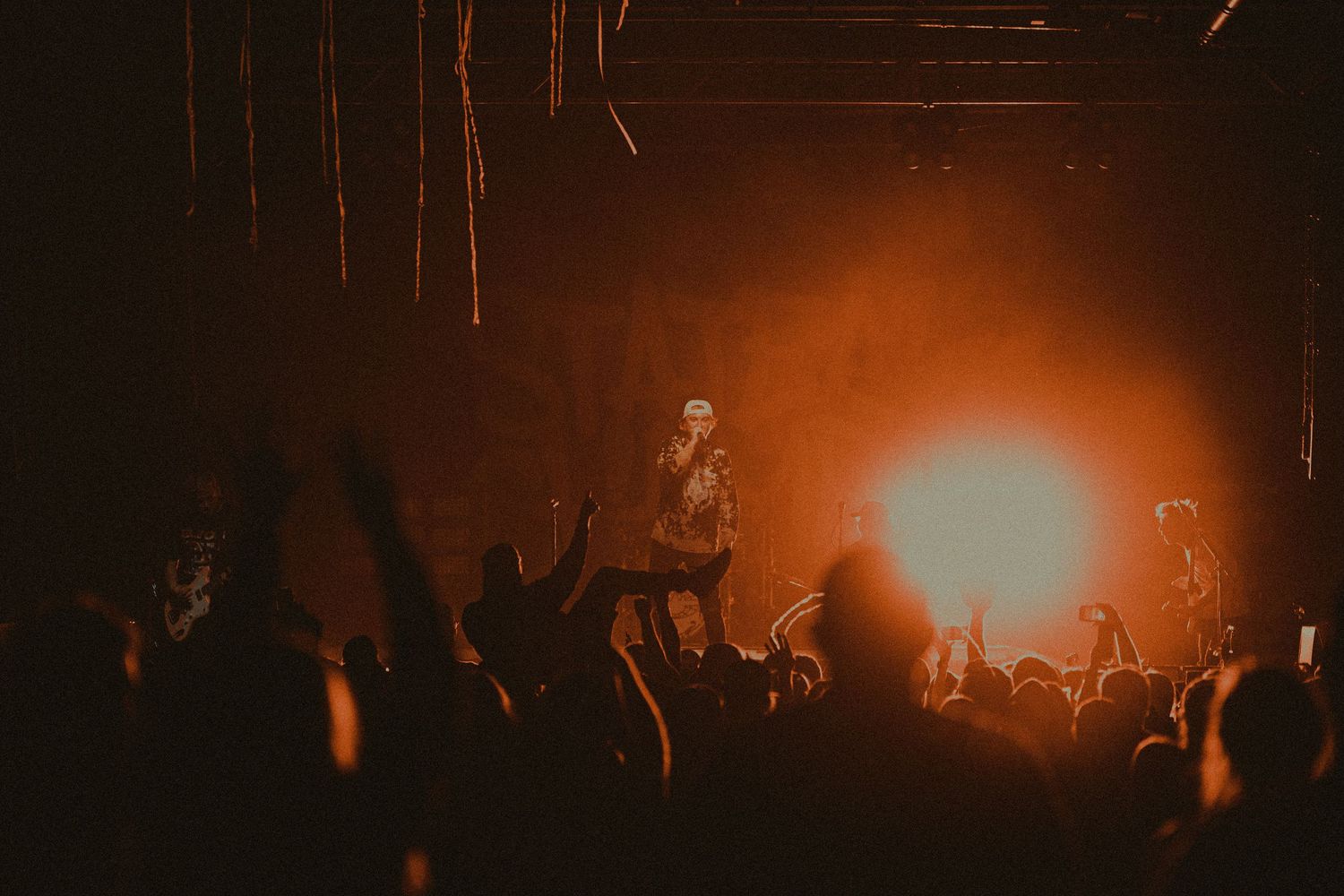 Concert crowd silhouettes against warm orange stage lighting creating an atmospheric live music scene.