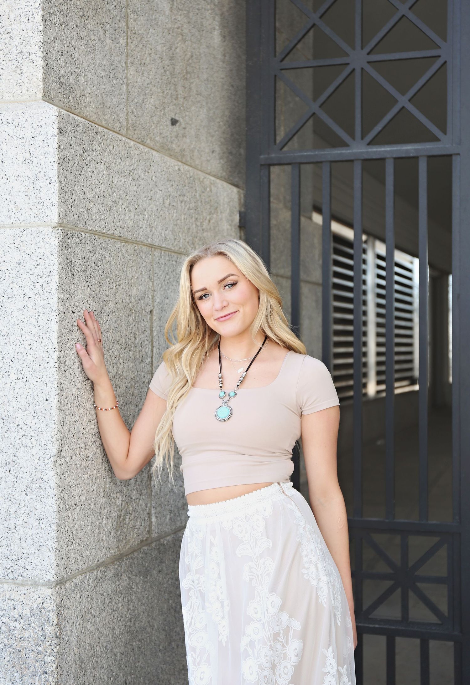 Person wearing a light-colored dress poses against a stone building with decorative windows.