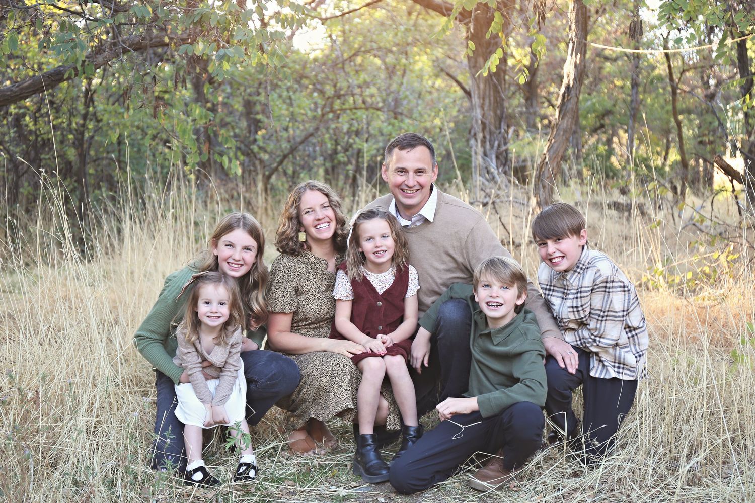 Extended family sits casually together in outdoor field during golden hour photo session.