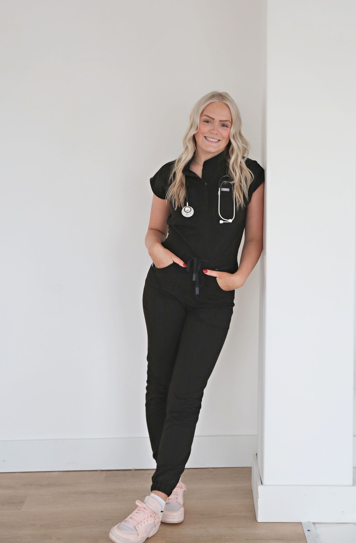 Healthcare worker in black scrubs poses playfully against white studio background.