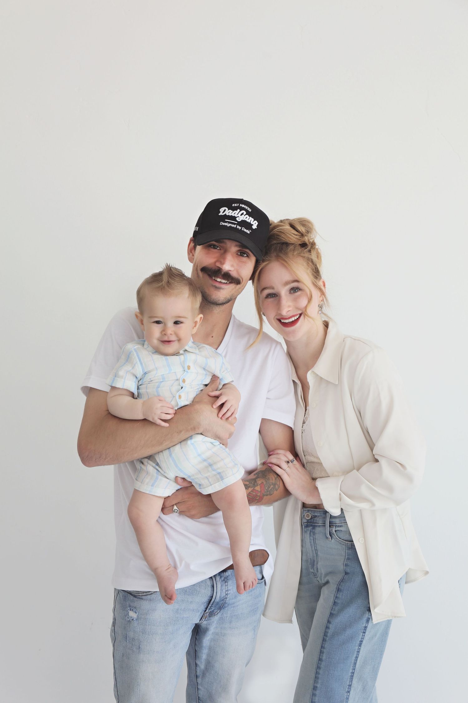 Small family poses together against white studio backdrop in coordinated casual outfits.
