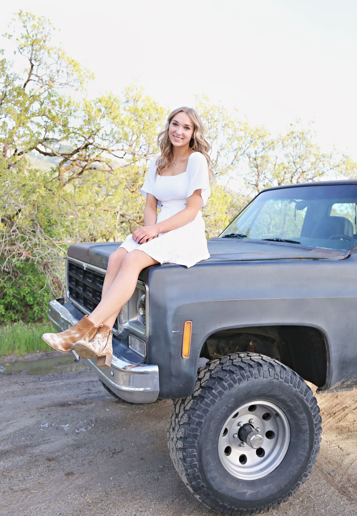 Portrait session with lifted truck featuring large off-road tires in natural setting.