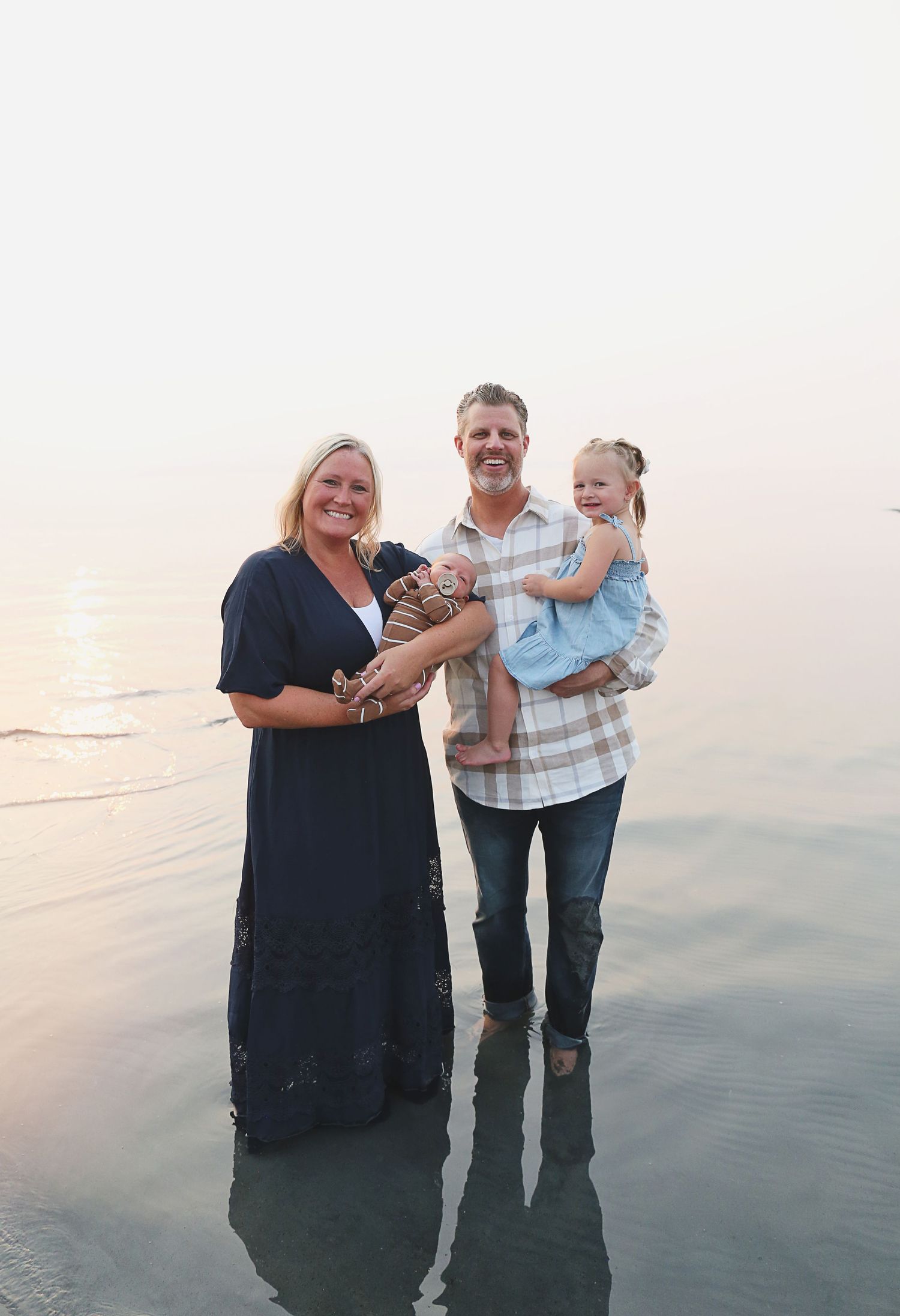 A family standing together in ankle-deep ocean water during sunset.