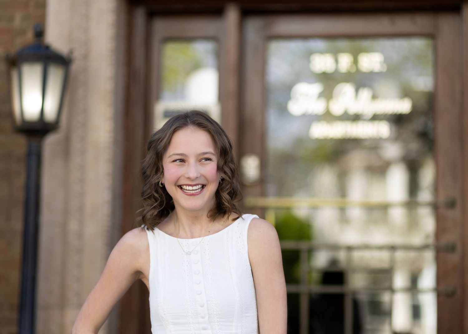 Smiling young woman in white dress standing in front of The Palomino restaurant entrance with street lamp.