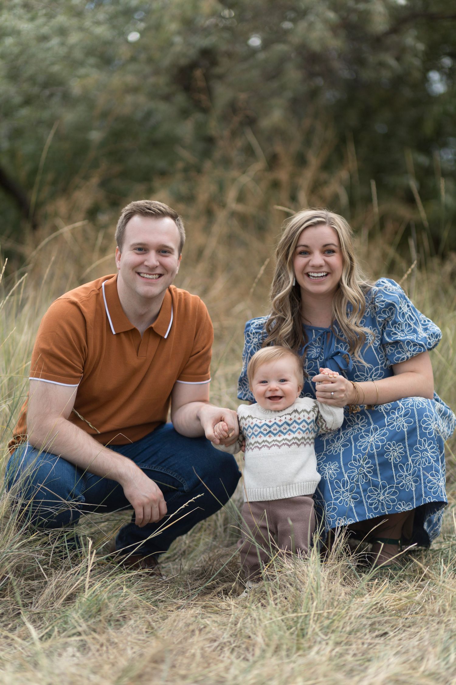 Family lying in tall grass field during outdoor photo session wearing blue and orange casual attire.