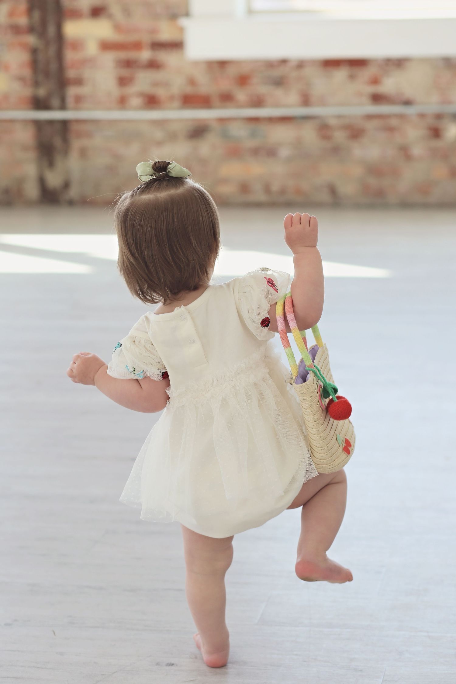 Baby in cream-colored dress taking first steps on white studio floor.