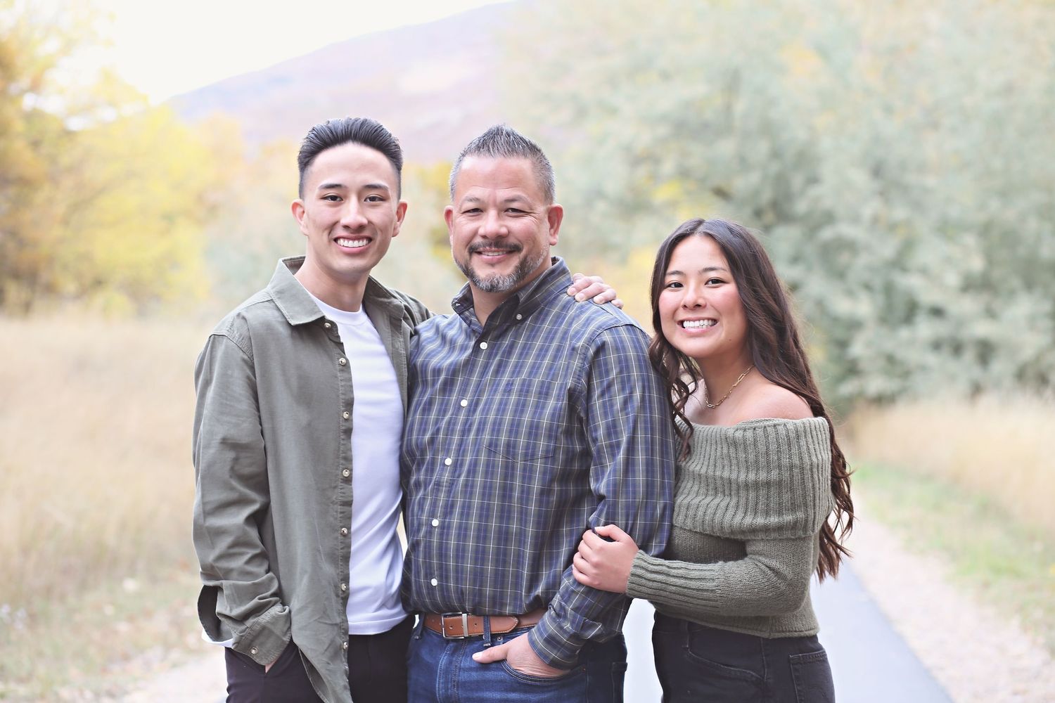 Family group poses together outdoors on a path during autumn with mountains and fall foliage in background.