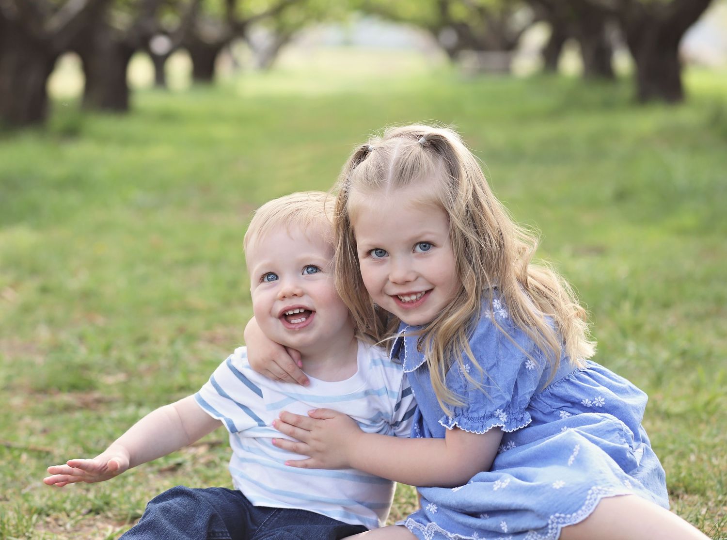Children playing and laughing together on grass under trees.
