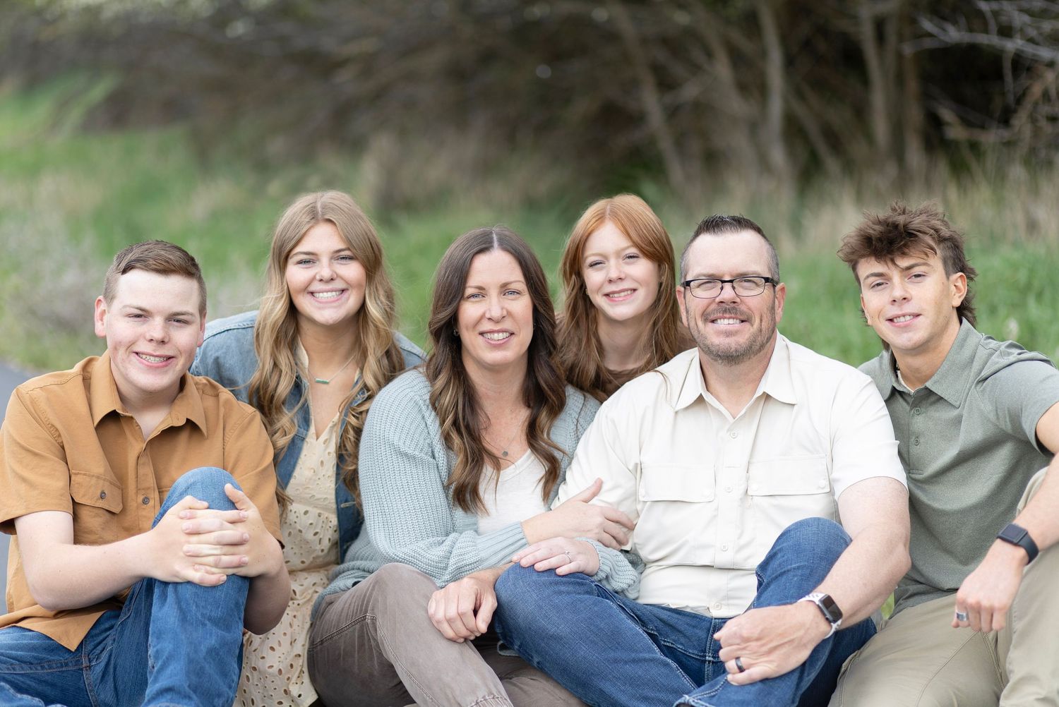 Happy family of six sitting together outdoors in a lush green setting.