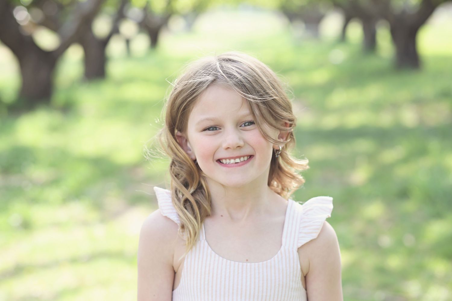 Cheerful outdoor portrait in white top with sunlit orchard background.