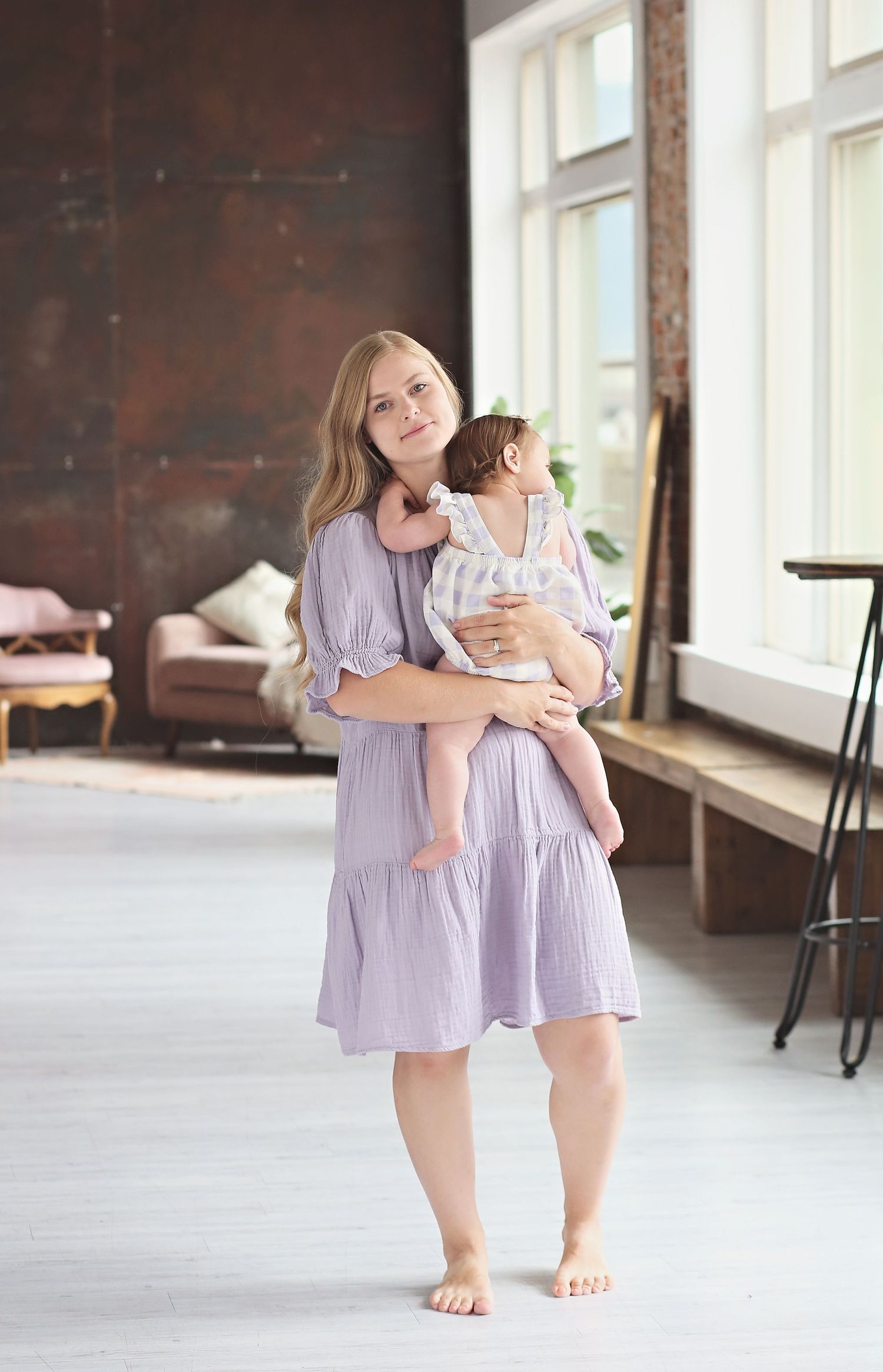 People wearing matching lavender dresses pose in a bright indoor space with brick walls.