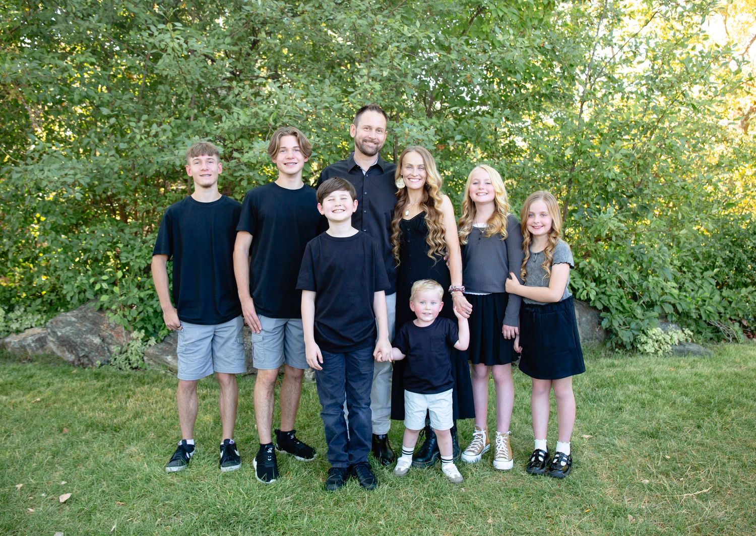 Large family group wearing coordinated black outfits posed together outdoors.