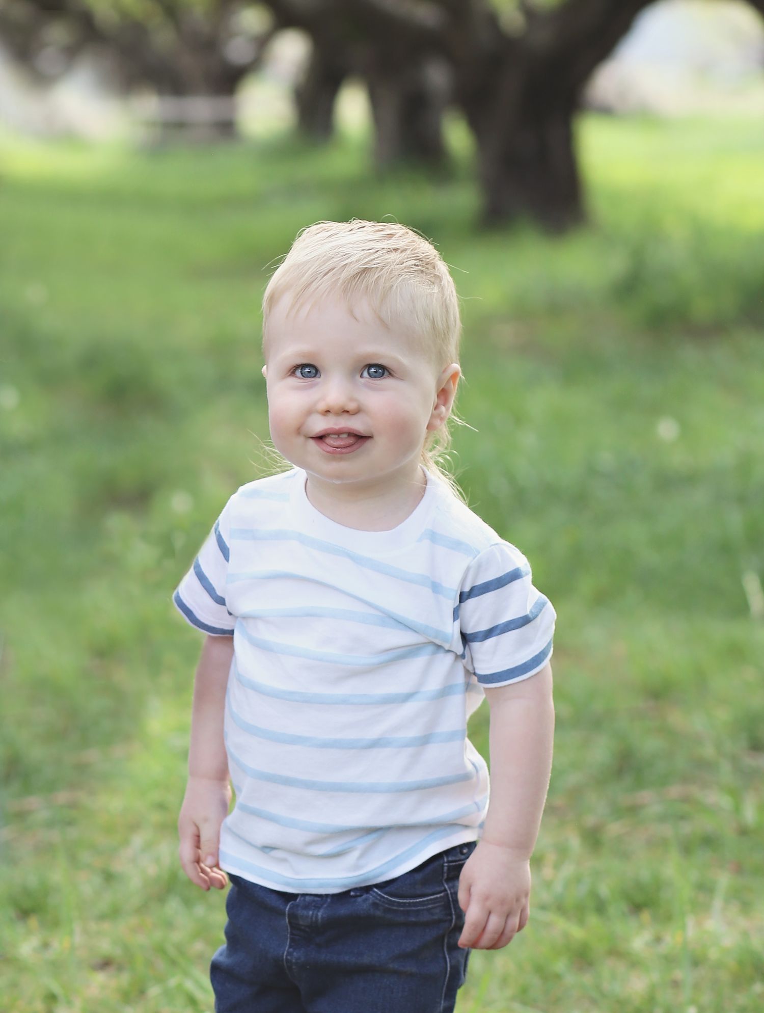 Toddler wearing white t-shirt with blue stripes and navy pants plays outdoors on grass.