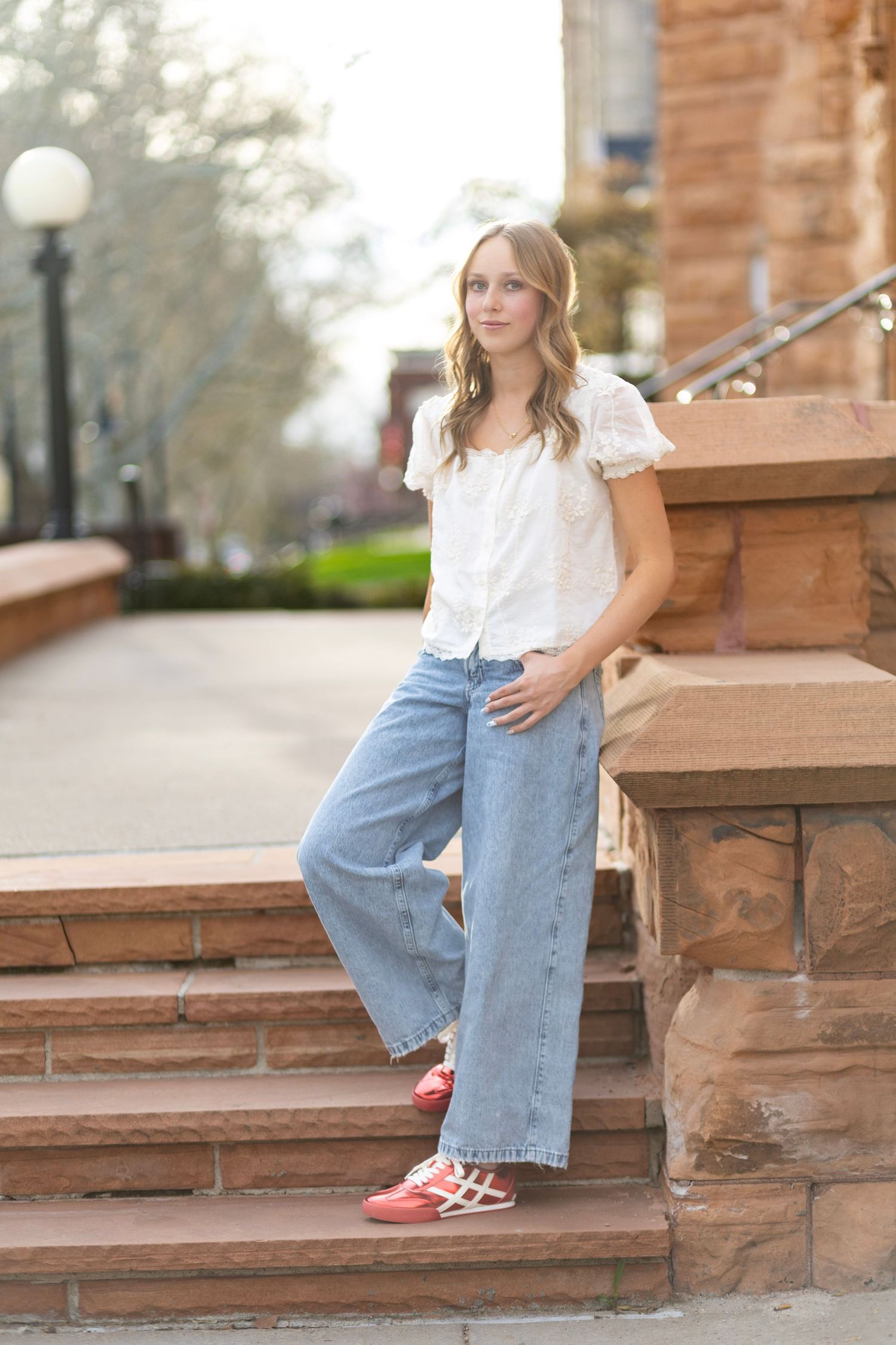 Young woman in wide-leg jeans and white blouse poses on stone steps outdoors.