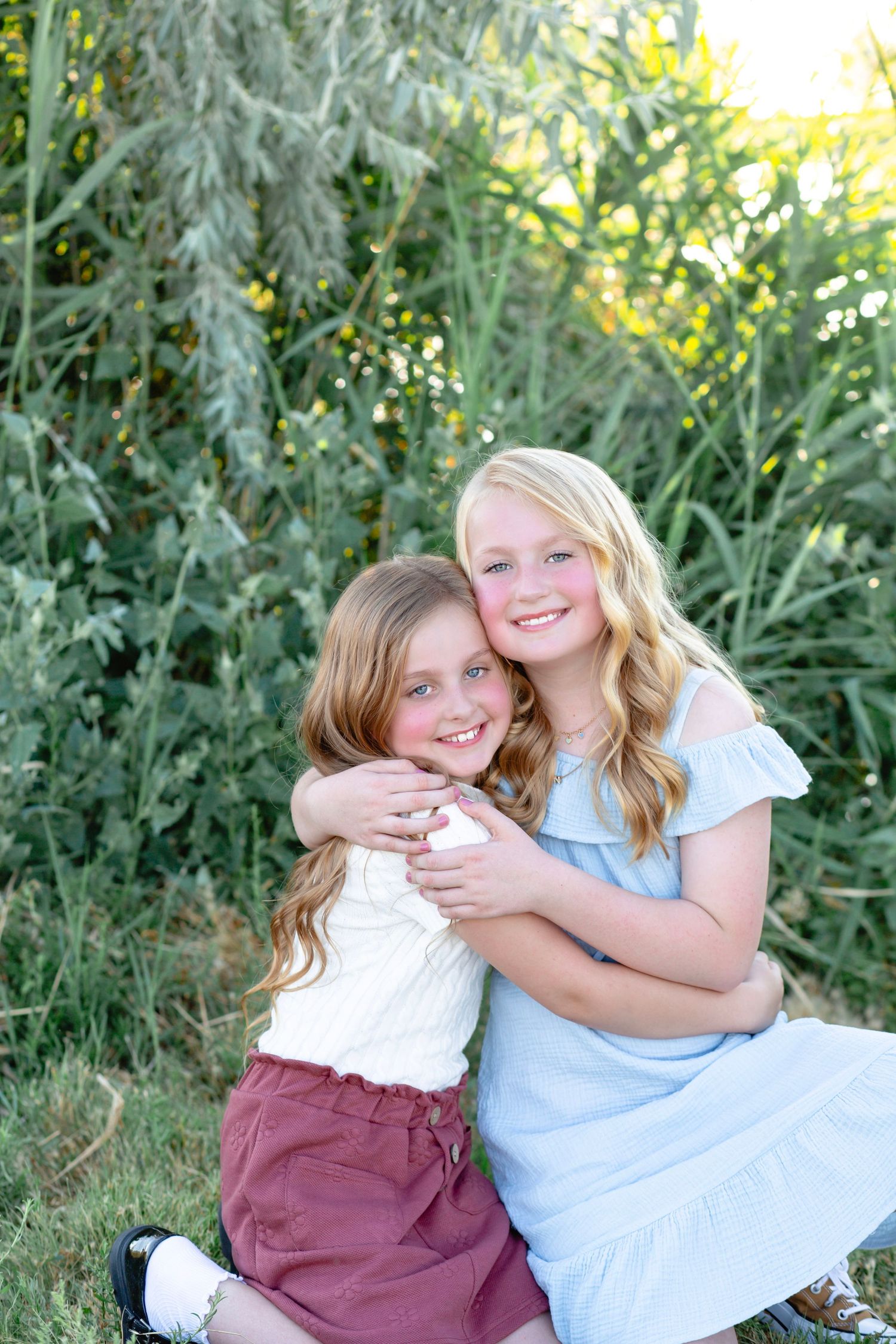 Two people share a warm embrace while sitting in tall grass on a sunny afternoon.