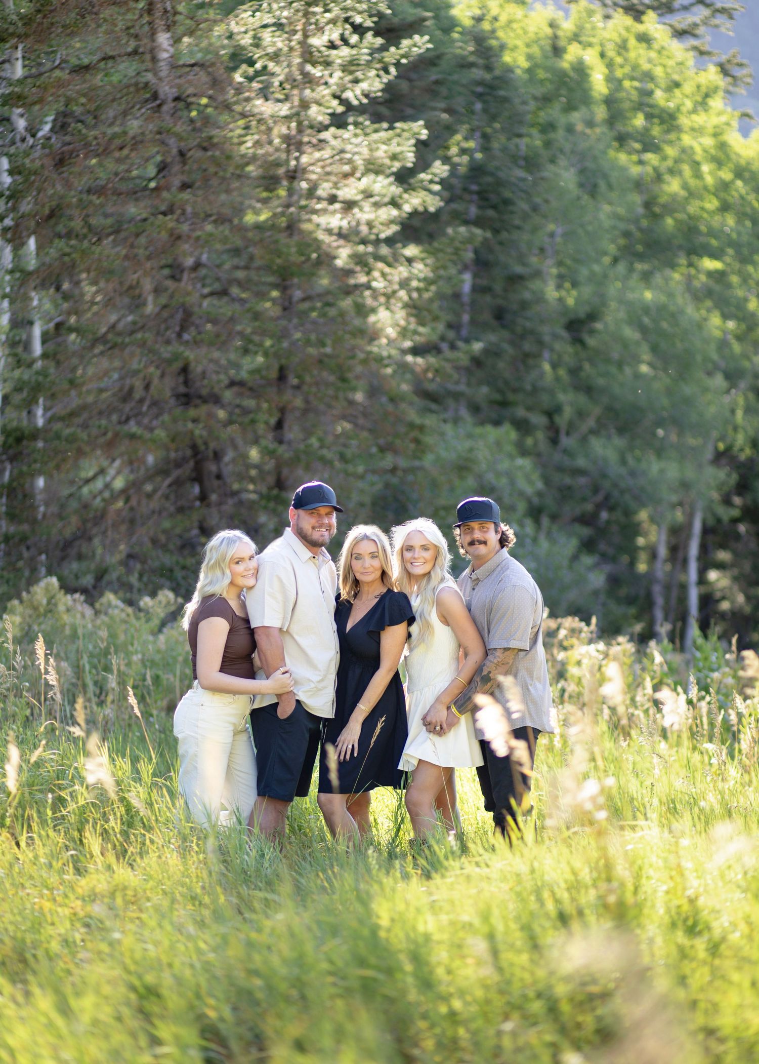 Family members gather in a sunlit meadow with tall grass and trees in the background.