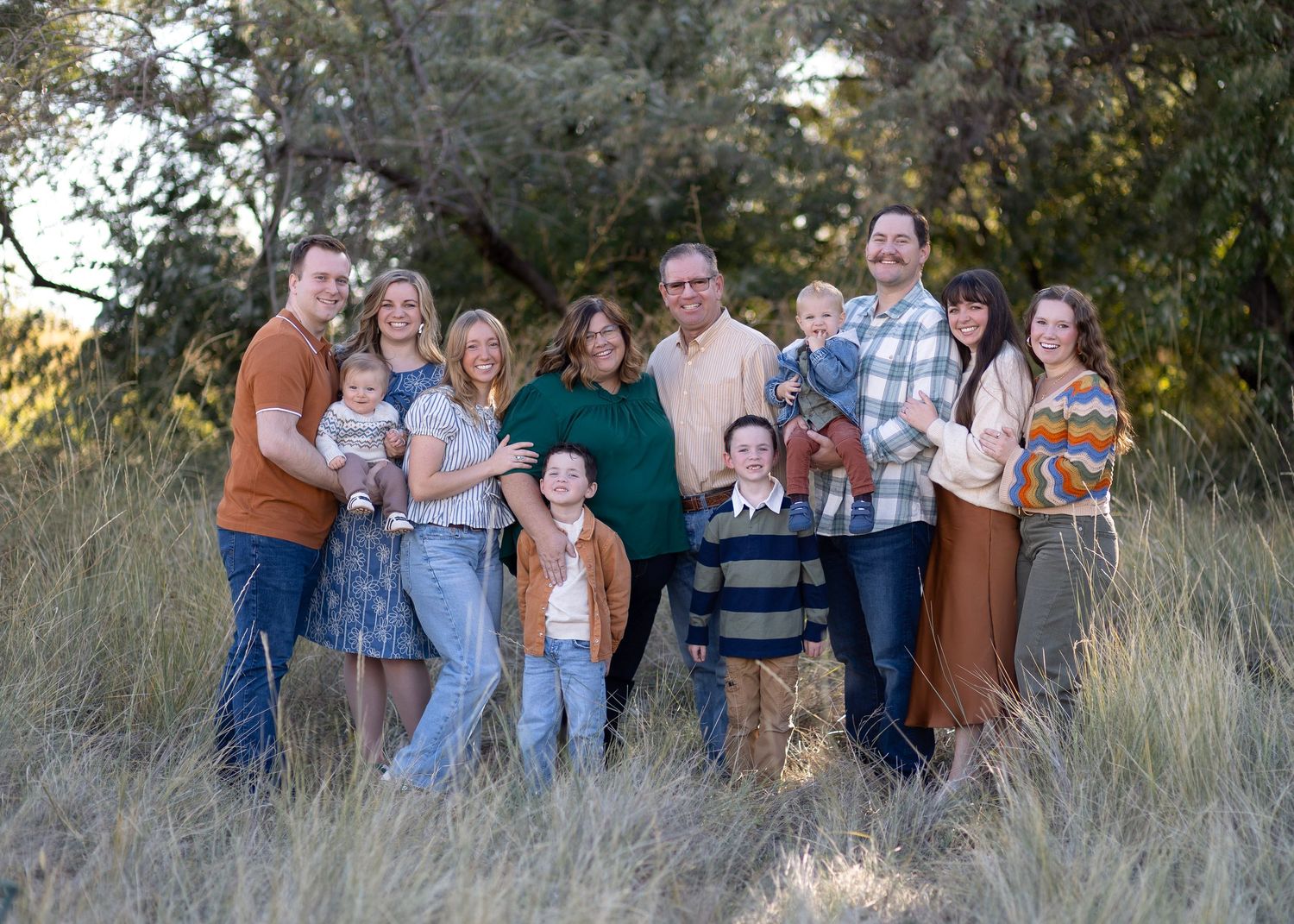 Extended family group photos in natural outdoor setting with tall grass and trees.